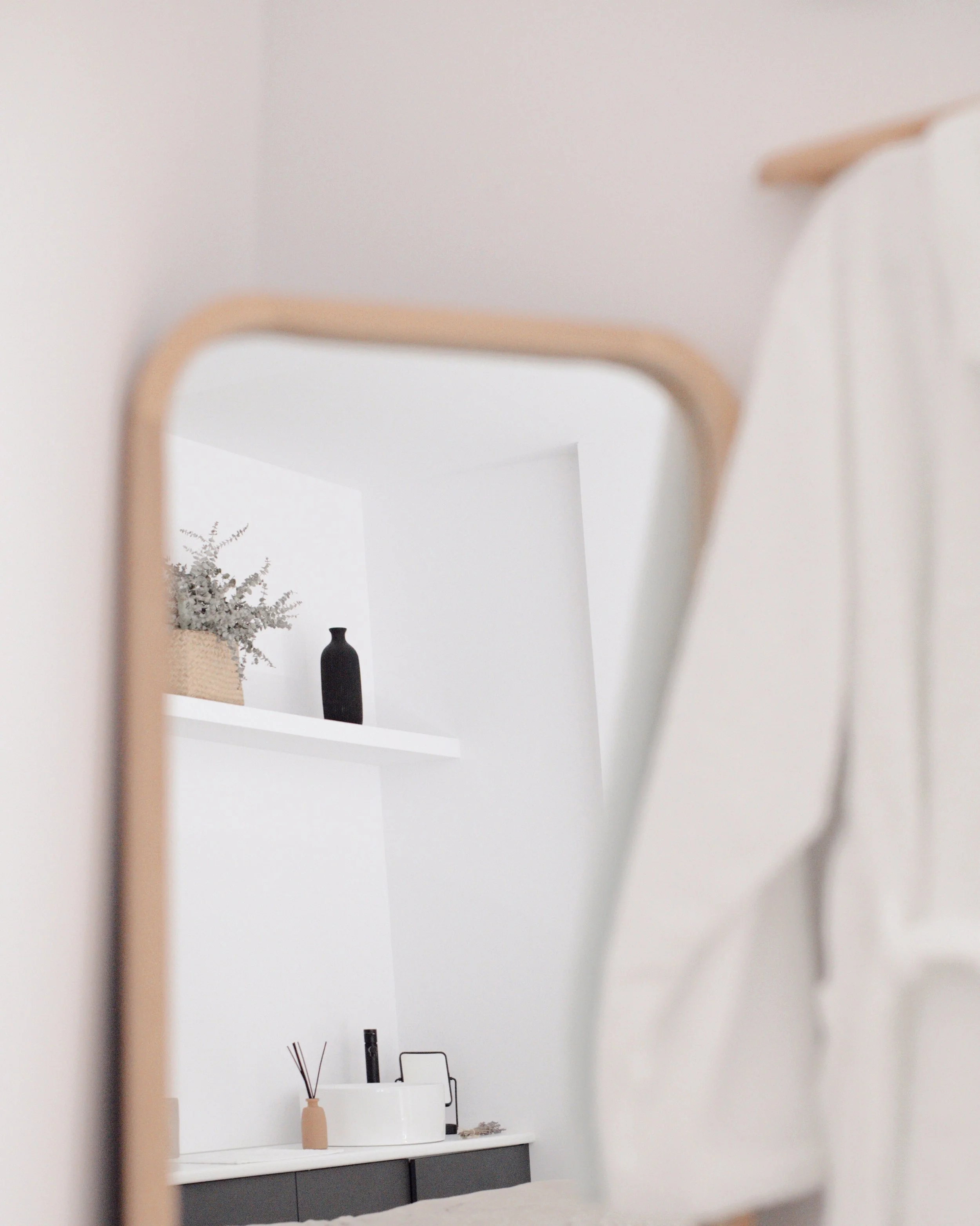 Espejo de cuerpo entero en primer plano en una habitación con decoración minimalista en tonos blancos y negros, con estantería blanca y accesorios decorativos.