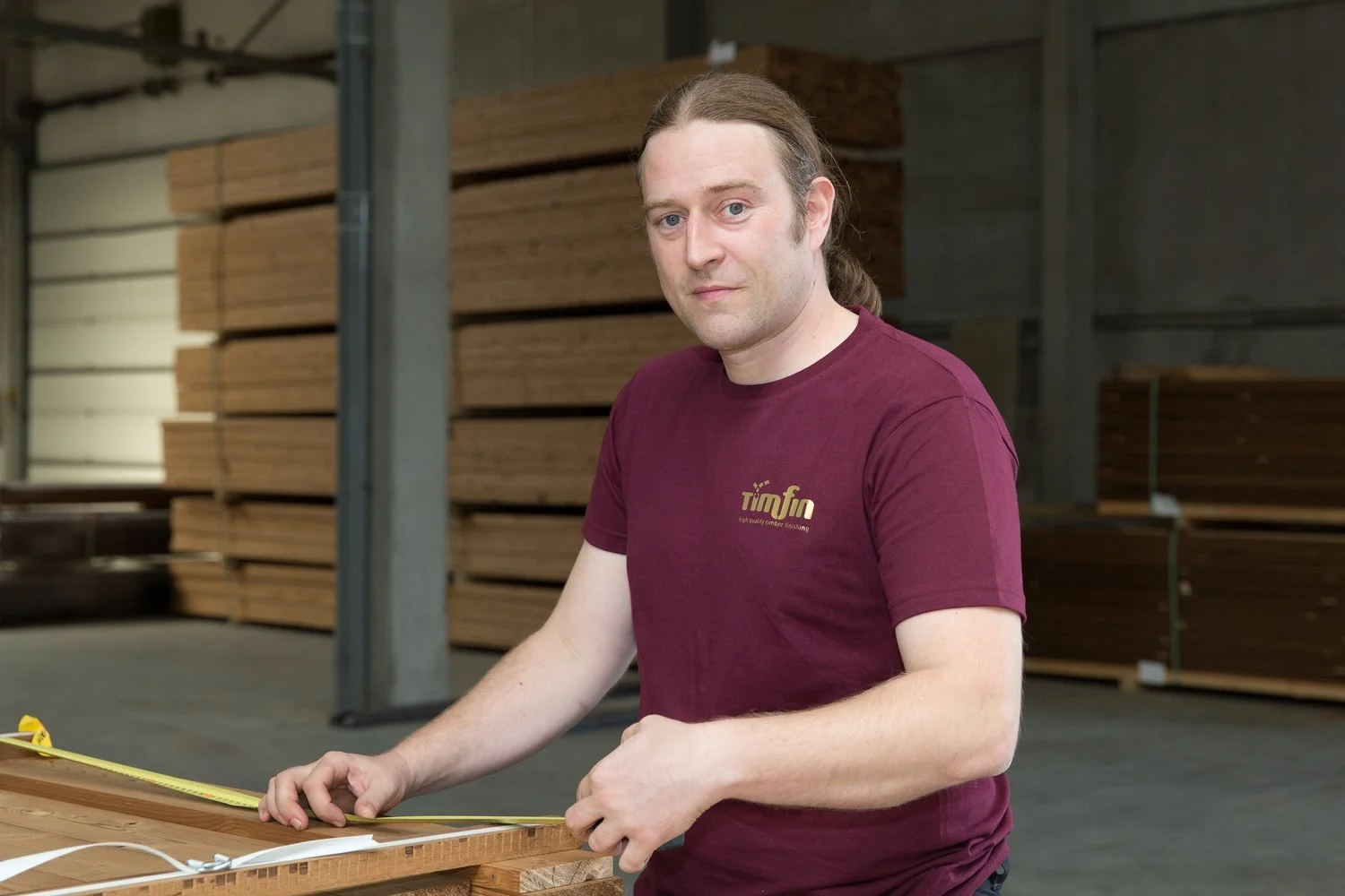 Man meet een gevelplanchet in een houtbewerkingsfabriek, met opgeslagen planken op de achtergrond.