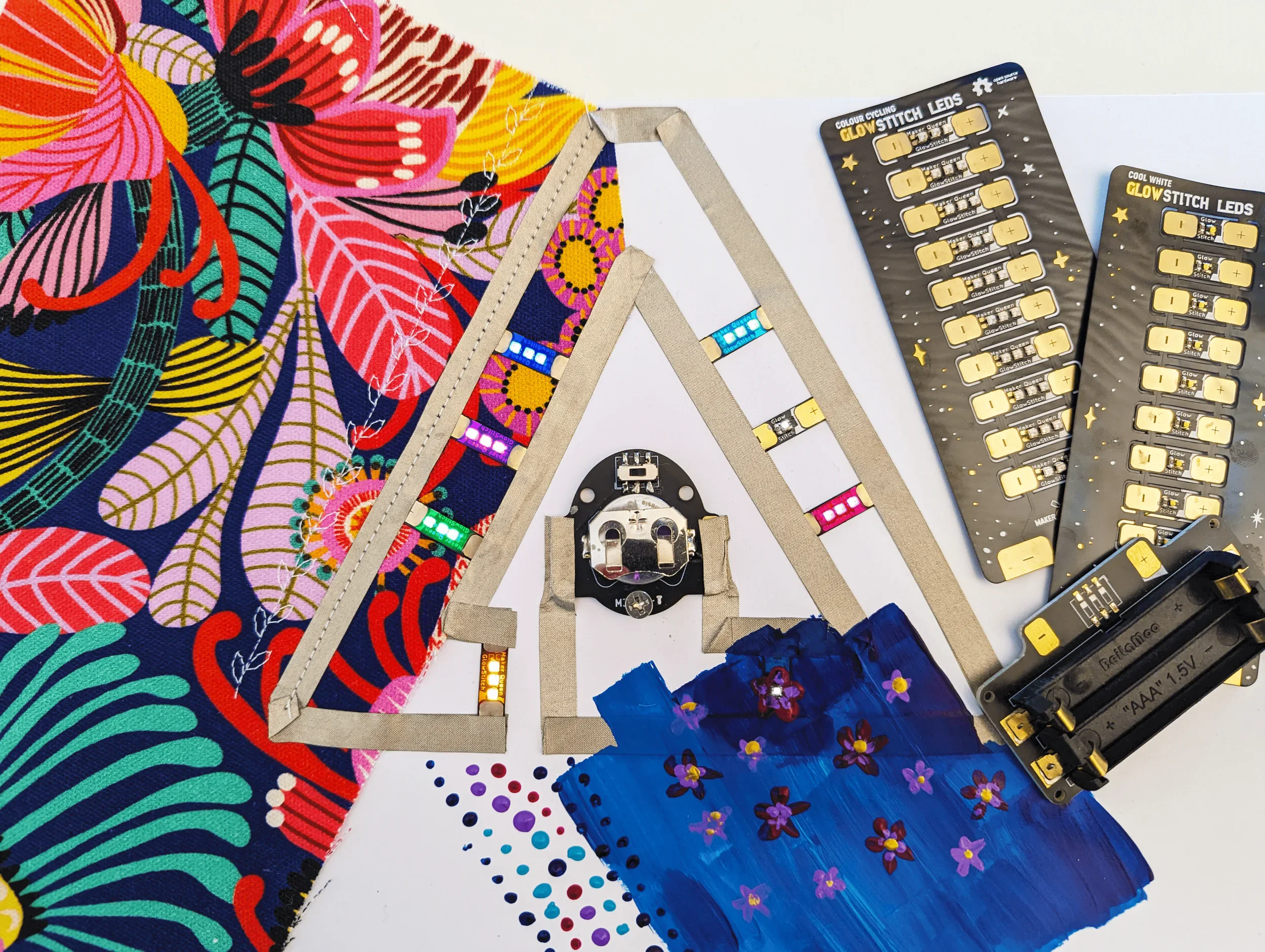 GlowStitch LEDs surrounded by fabric, cardboard, battery holder, and electronic components.