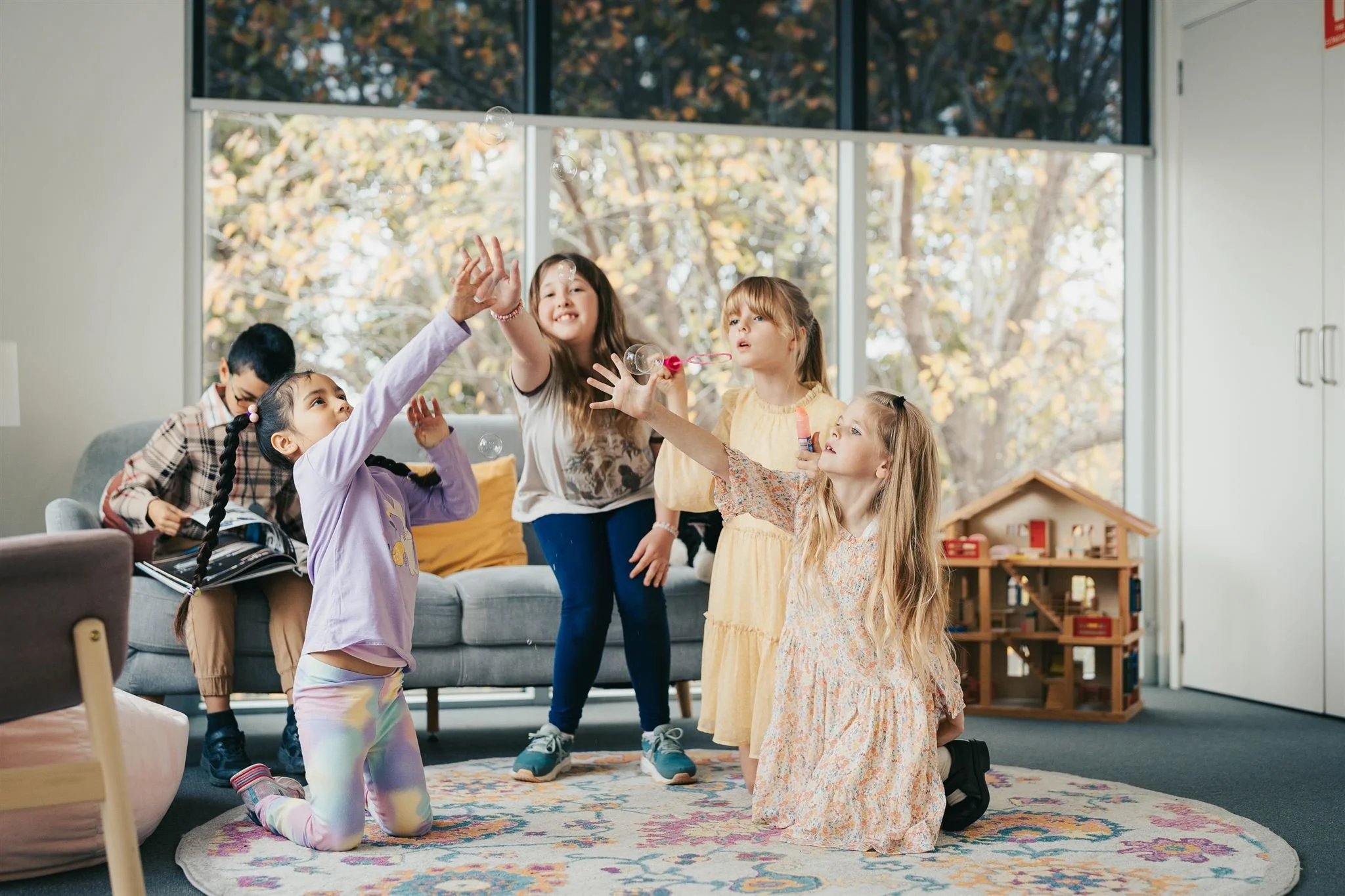 Unedited version of Children playing with bubbles indoors with large windows and a view of trees outside.