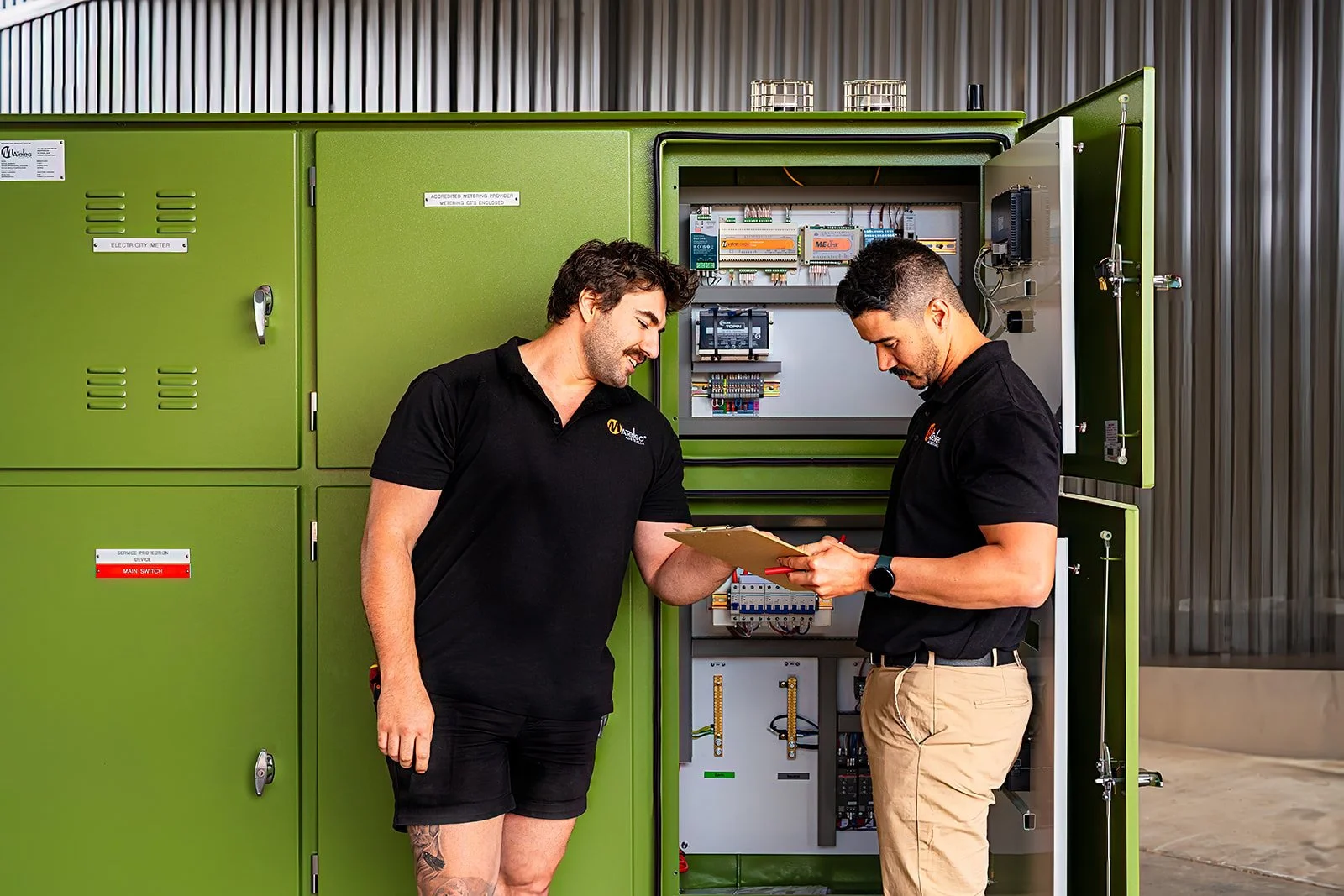 Two workers discussing notes in front of electrical switch panel just after installation