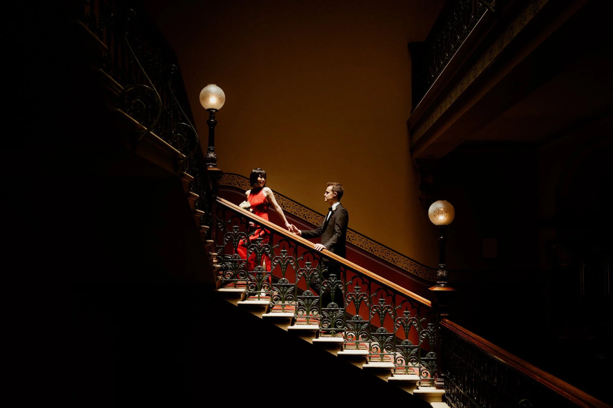 A couple walking up the iconic stairwell in a shaft of light in the Windsor Hotel Melbourne