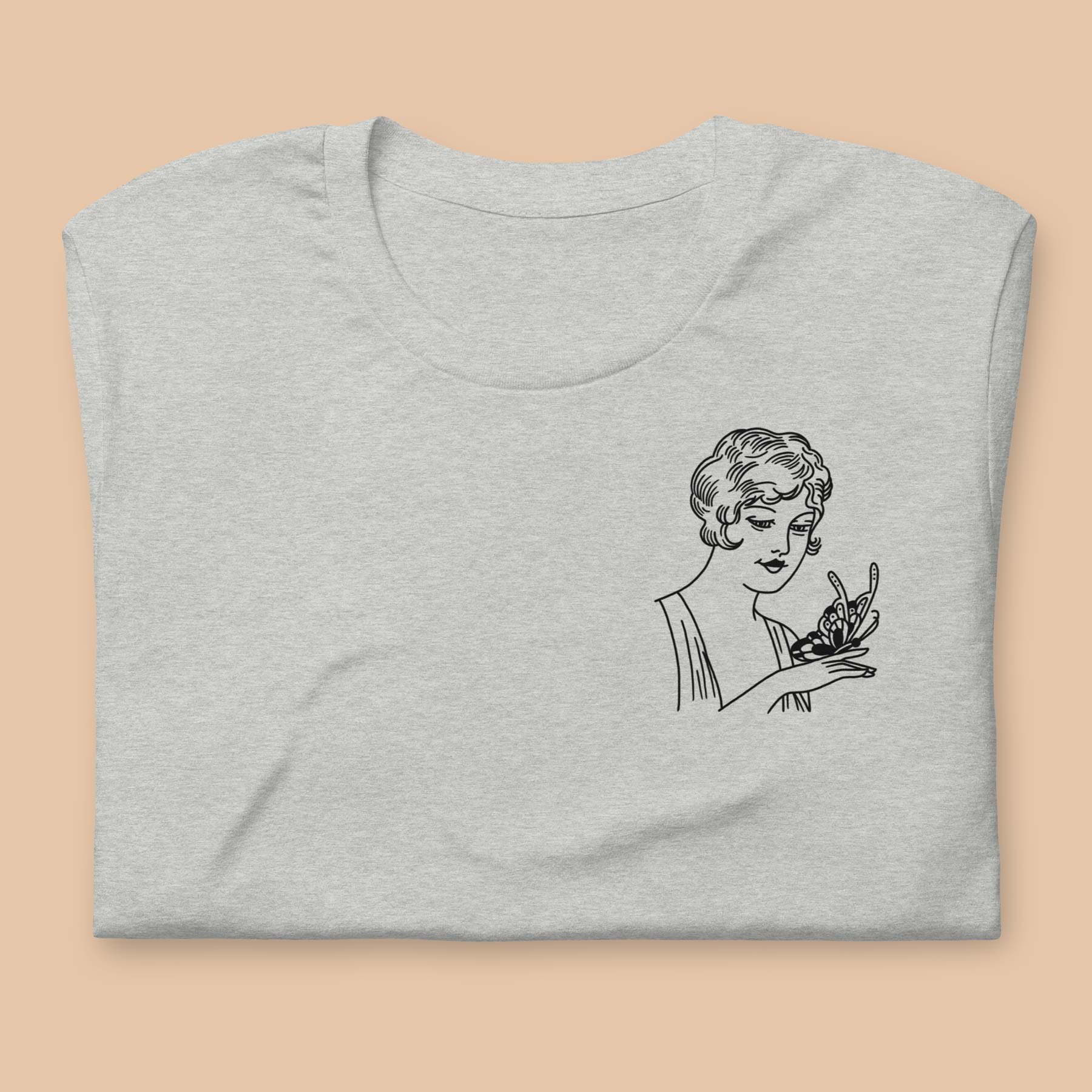 Heather grey t-shirt with chest priint of a tattoo design folded flat on a peach background.