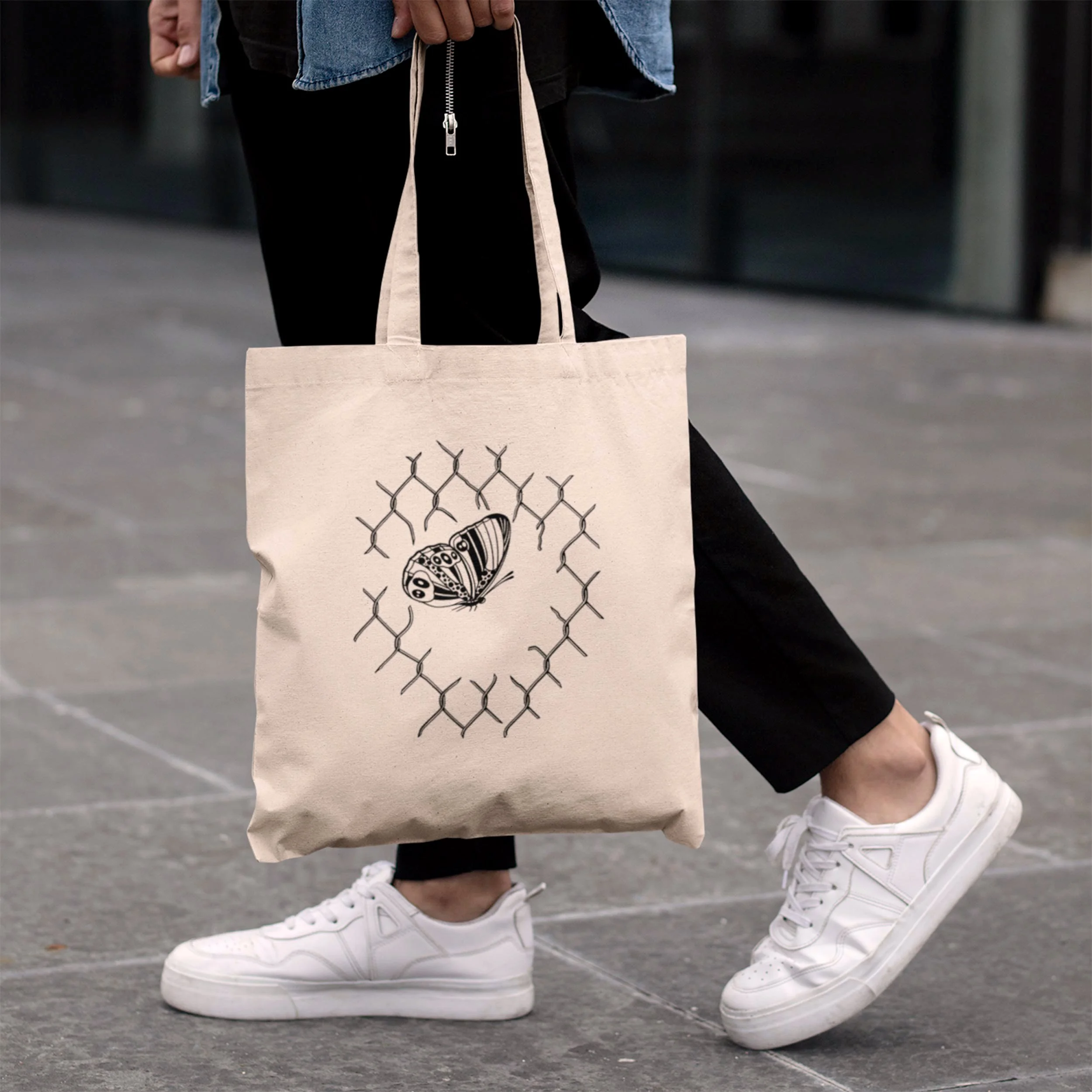 Model-wearing-black-pants-and-denim-shirt-holding-a-tan-tote-with-tattoo-design-one-one-side.jpg