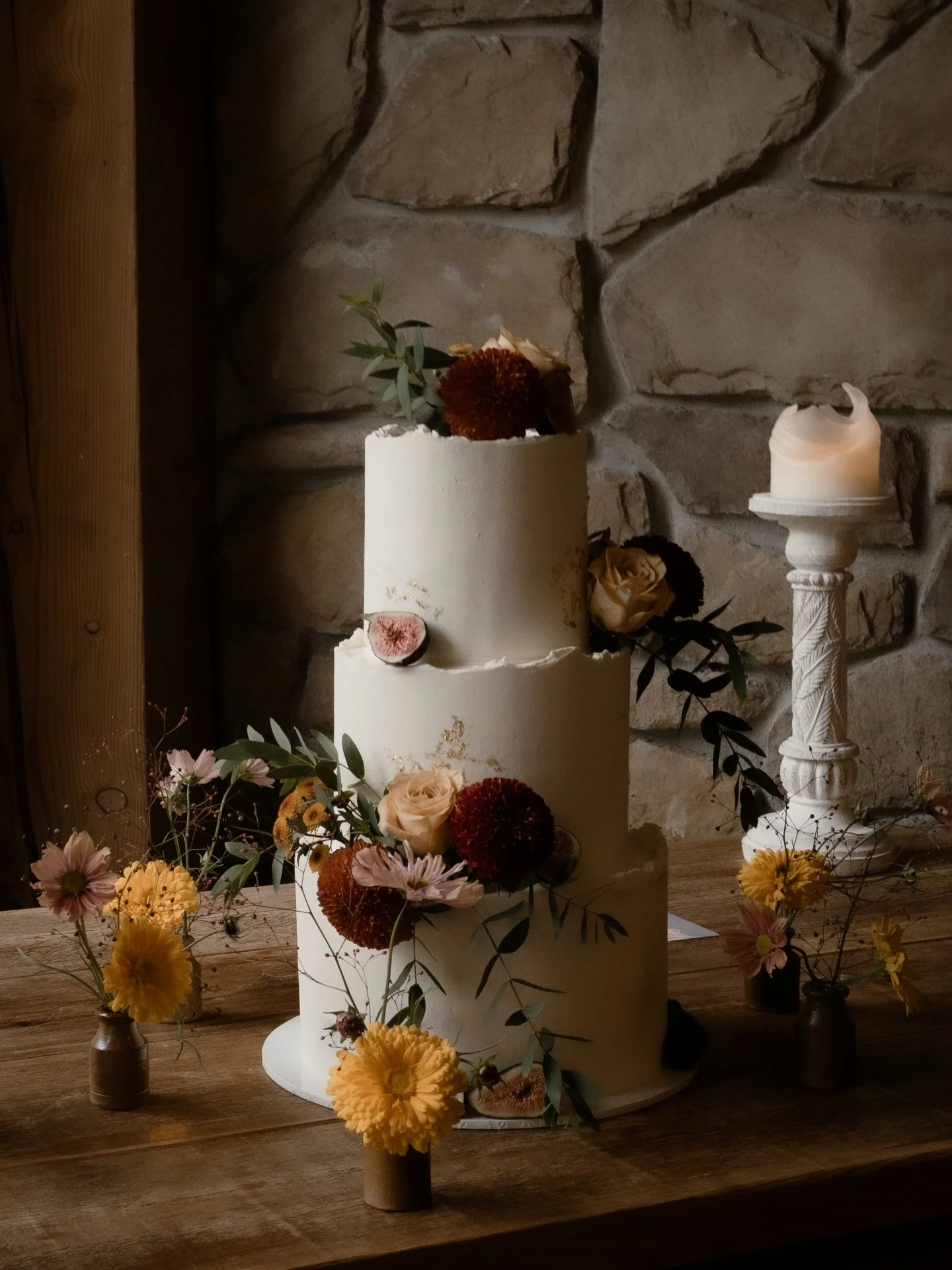 A closer look at Selena &amp; Keelan&rsquo;s three-tier autumn wedding cake. A design shaped by natural texture and gentle luxury. Torn-edge buttercream, touches of edible gold leaf, and clusters of figs, roses, dahlias and cosmos in warm, tonal shad