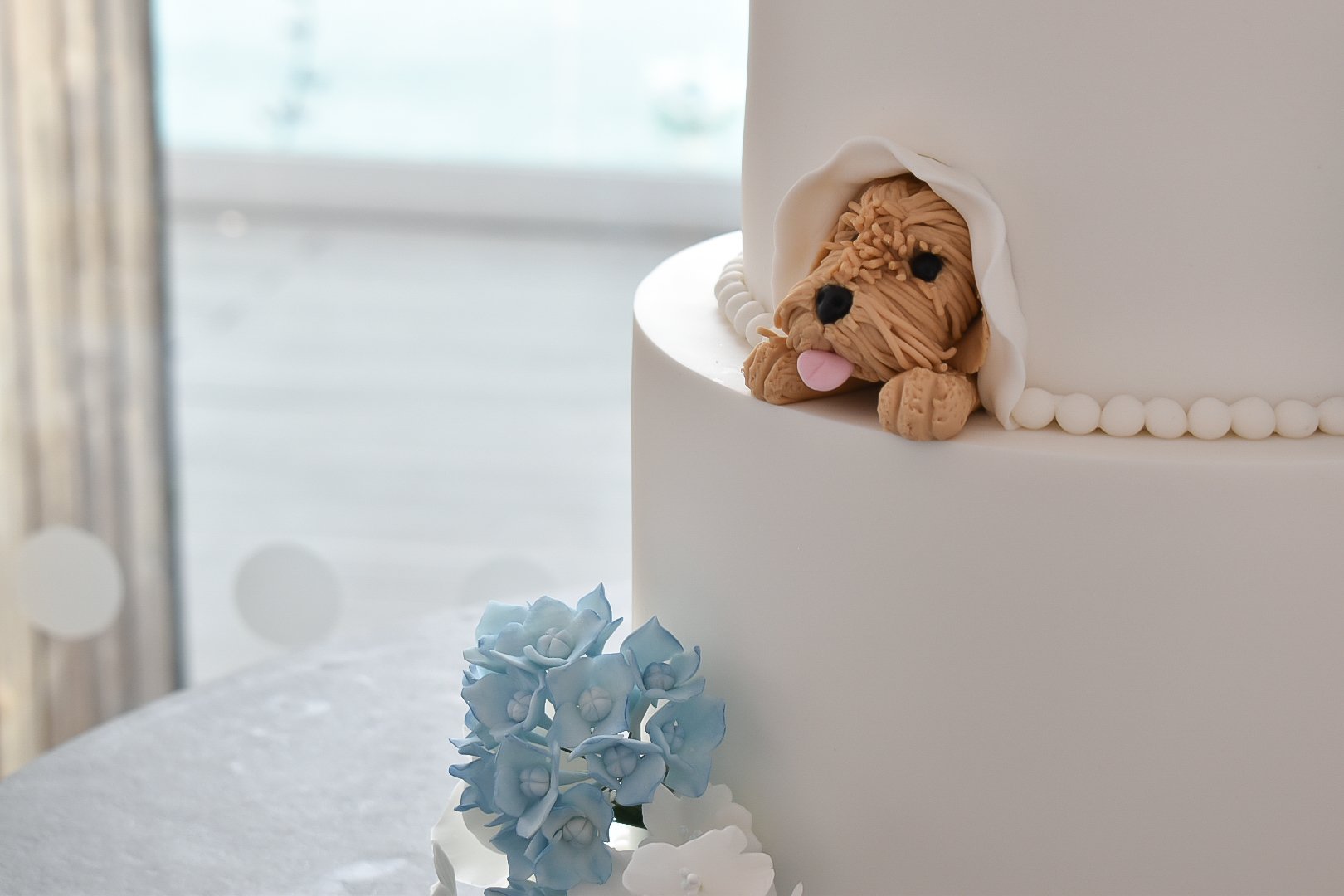 Handmade cockapoo dog on a white wedding cake with handmade sugar flowers at Sandy Cove Hotel.