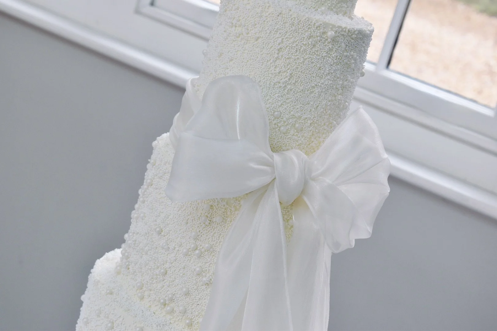 Tiered pearl wedding cake with large organza bow.