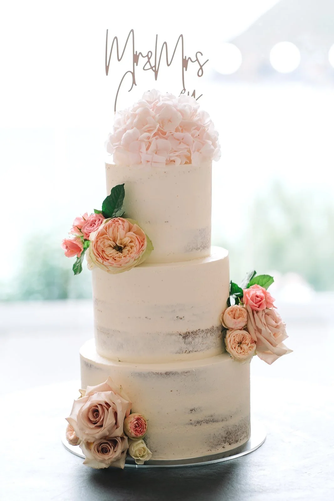 pastel coloured fresh flowers on a semi-naked wedding cake.