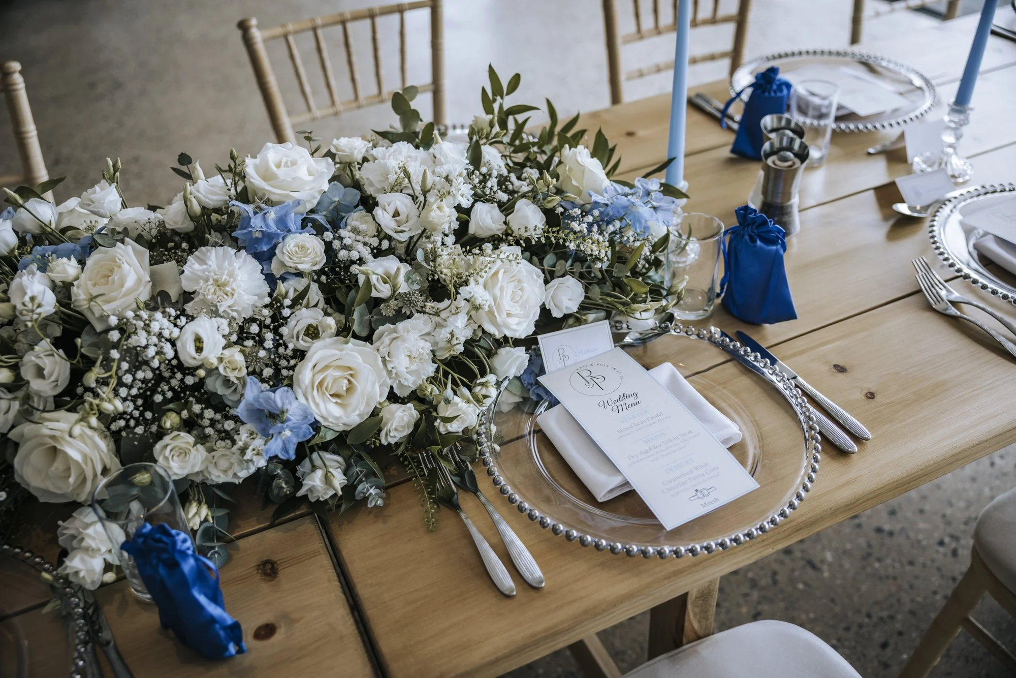 Modern coastal wedding tablescape with roses, delphiniums and blue taper candles