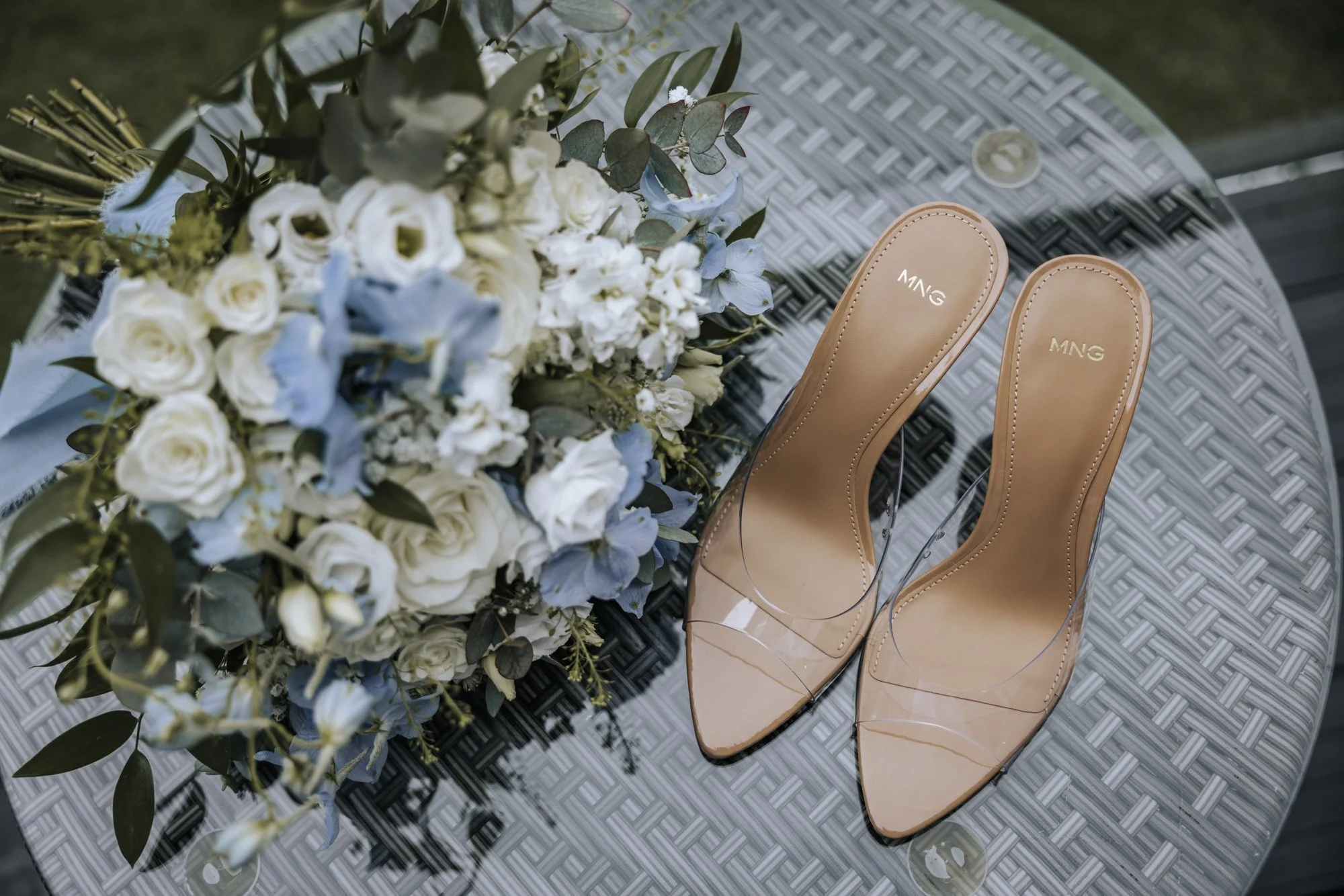 Ivory and powder-blue bridal bouquet with eucalyptus beside clear-strap nude heel