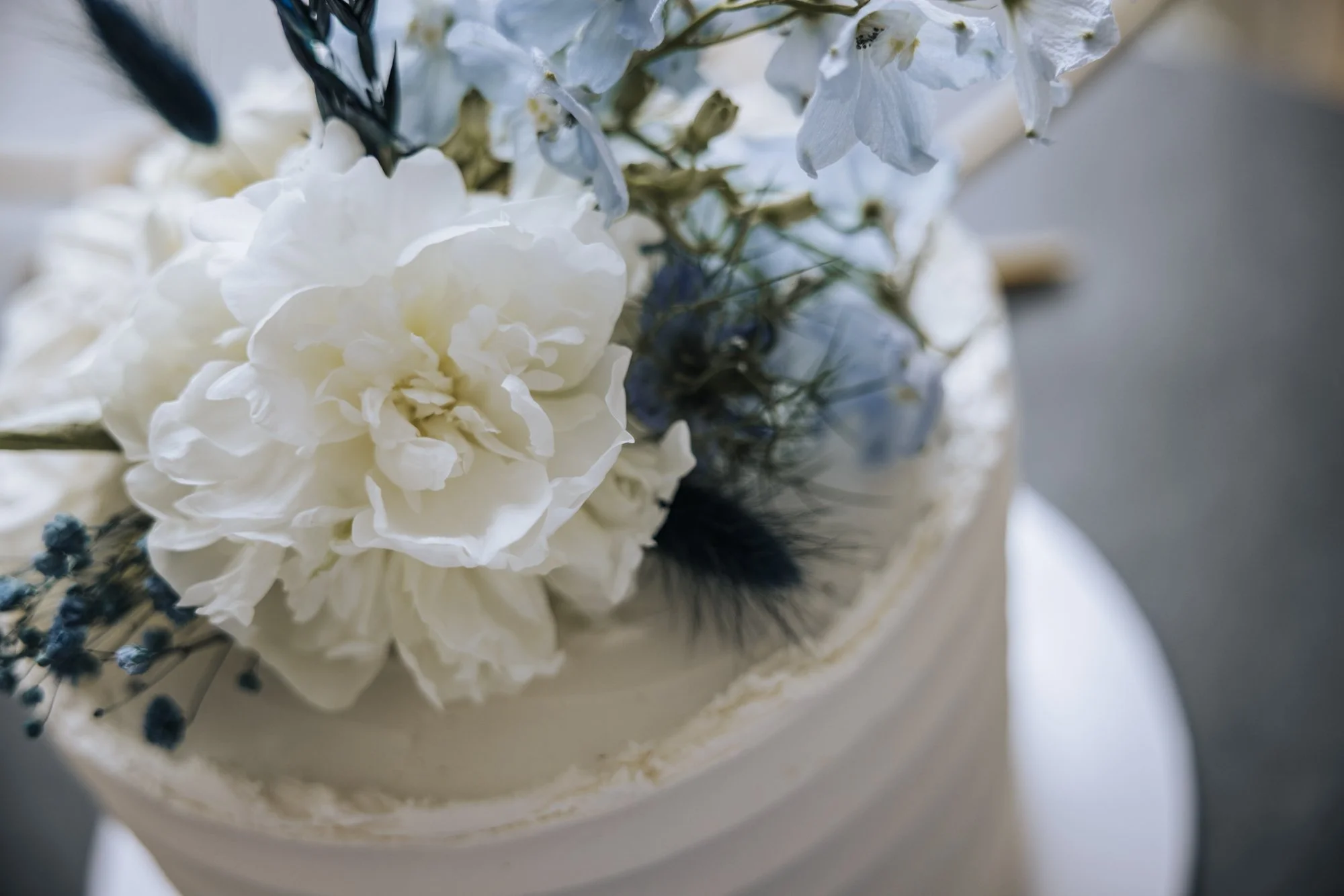 White buttercream cake finished with blue and white fresh flowers.