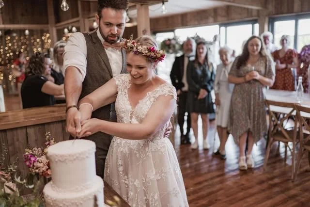 Boho Couple cutting a pearl wedding cake in a rustic barn.
