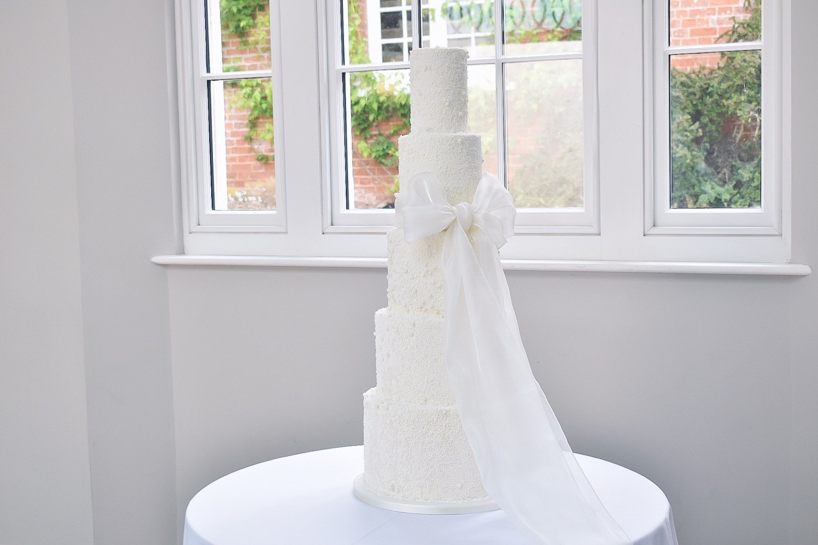 Tiered wedding cake with pearl detail and large organza bow at Rockbeare Manor.