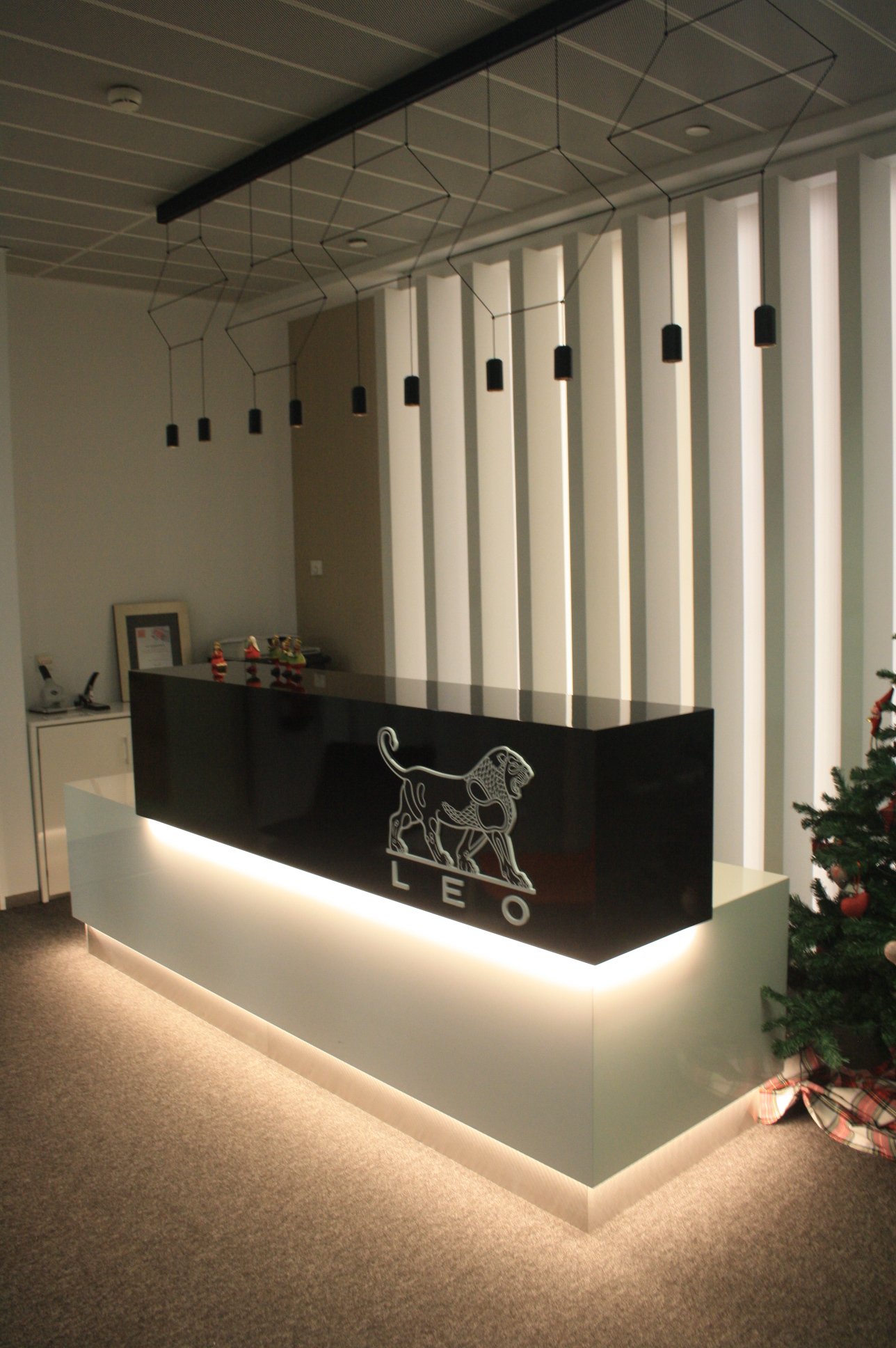 Balcão de recepção com iluminação integrada, candeeiro suspenso e painel ripado retro iluminado.