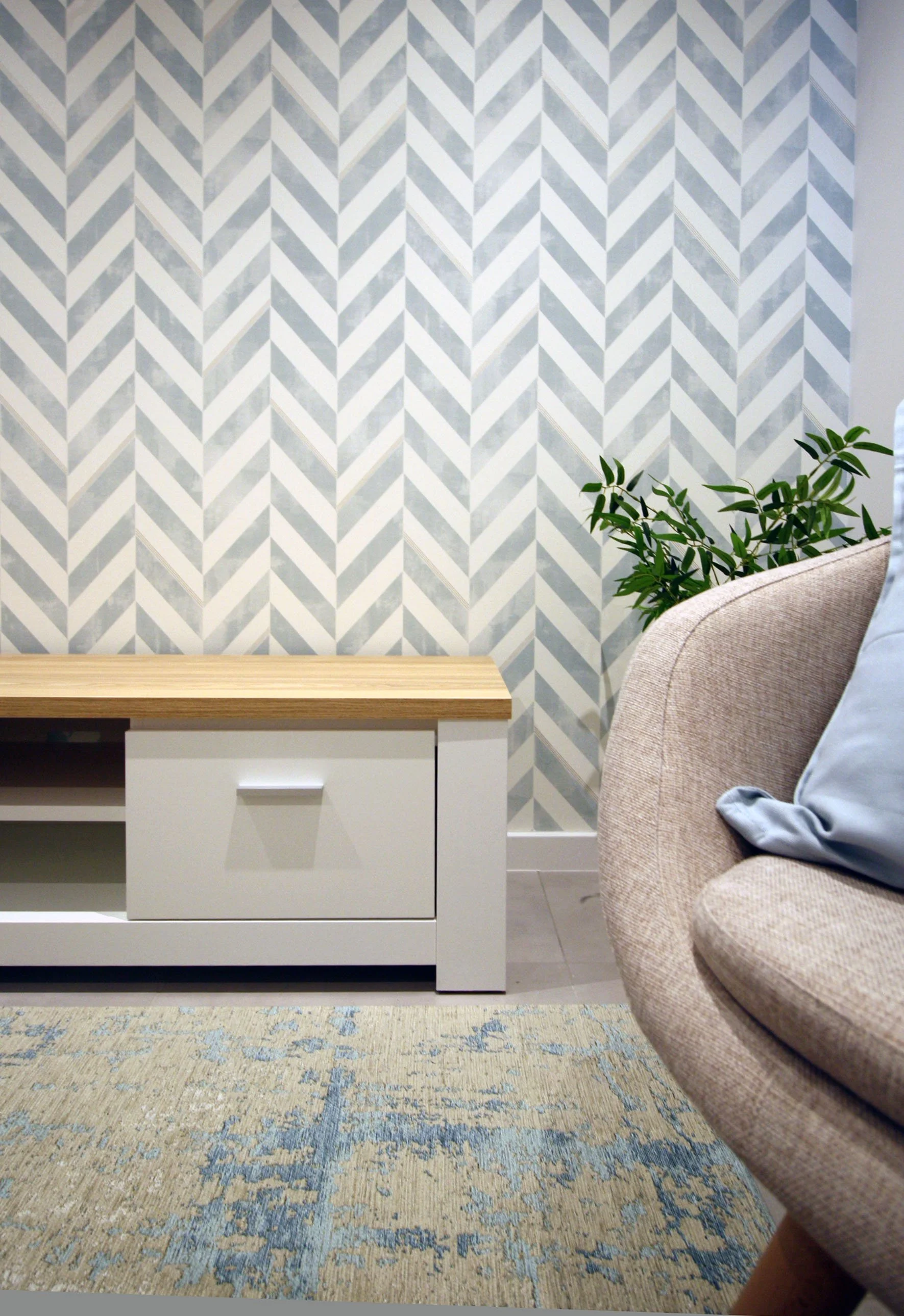Home Staging de Apartamento em Quarteira, Algarve.
Sala de estar moderna com sofá cinza, almofadas azuis e quadros de praia na parede, incluindo fotos de palmeiras, praia e oceano. Aplicação de papel em parede de TV. Decoração clean num ambiente repl