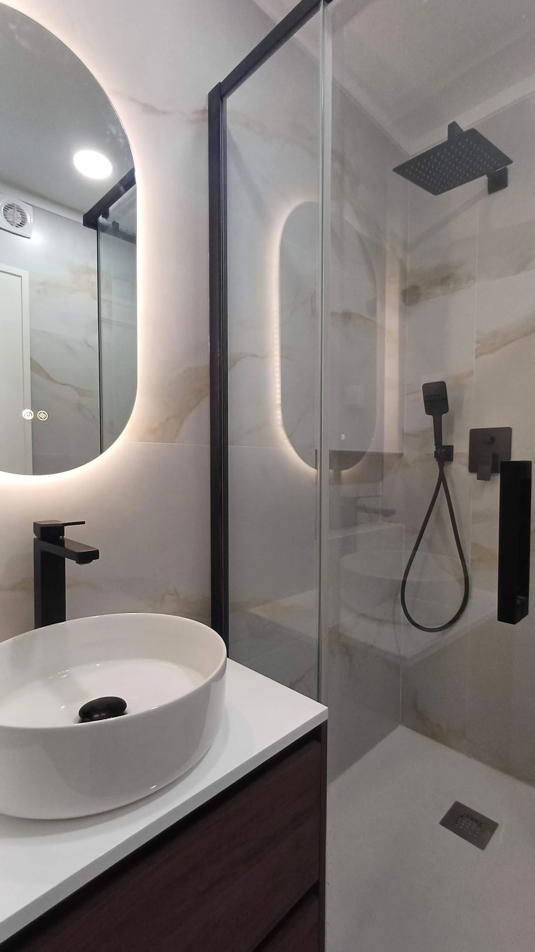 Projeto de Interiores e Remodelação de Apartamento, Queluz.
Remodelação de Casa-de-Banho com revestimento marmoreado de laivos dourados, Armário suspenso em madeira de Nogueira, acessórios em preto e espelho de forma oval com iluminação integrada.