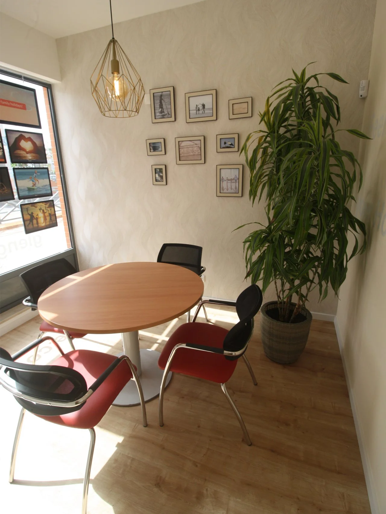 Sala de reunião com mesaredonda de madeira, quatro cadeiras estofadas com estrutura metálica. Parede com molduras e fotos.