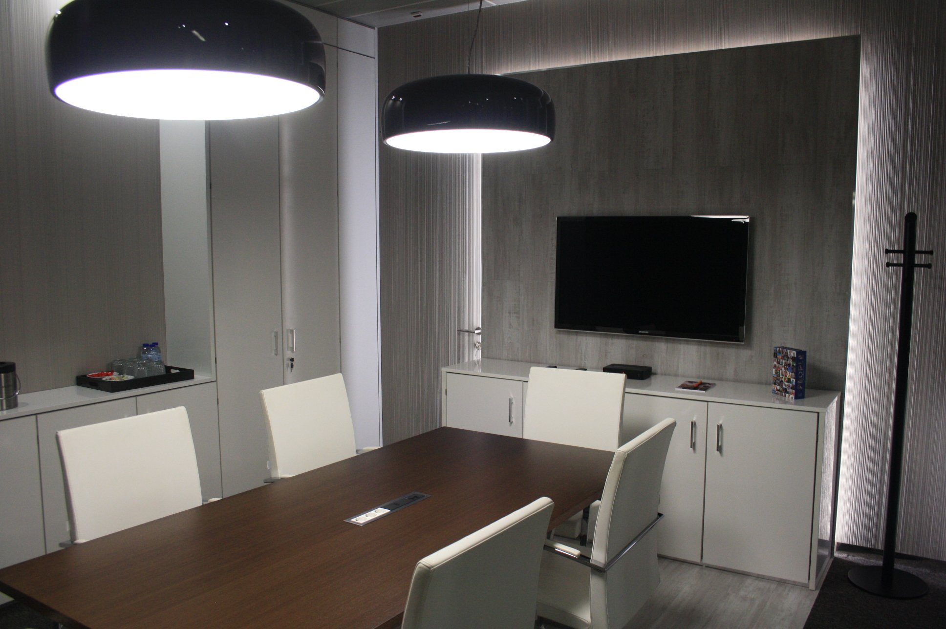 Sala de reuniões com painel retroiluminado, candeeiros de teto e cadeiras estofadas a pele branca.