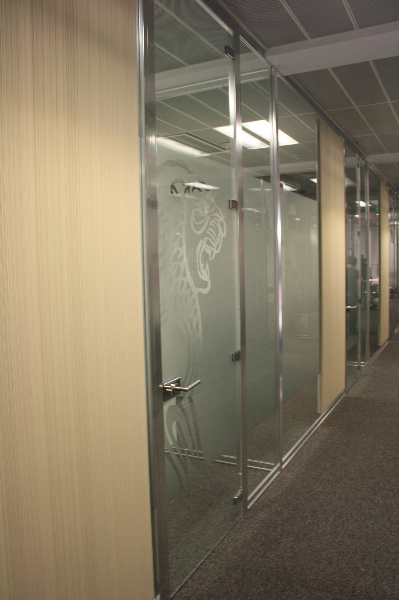 Corredor com divisória em vidro, decoradas a vinil frost e apontamentos revestidos a vescom.