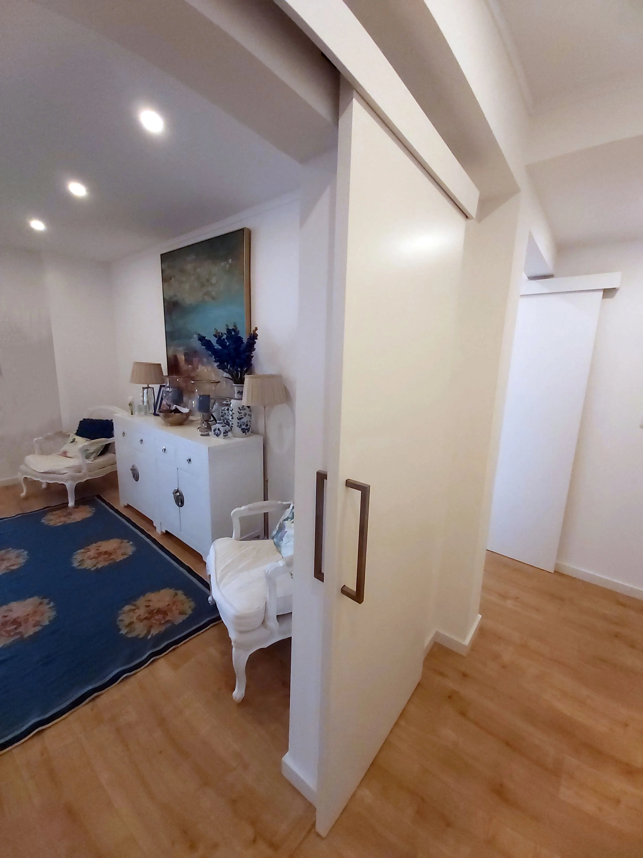 Hall e corredor com portas de correr com acabamento lacado a branco e pavimento flutuante carvalho natural