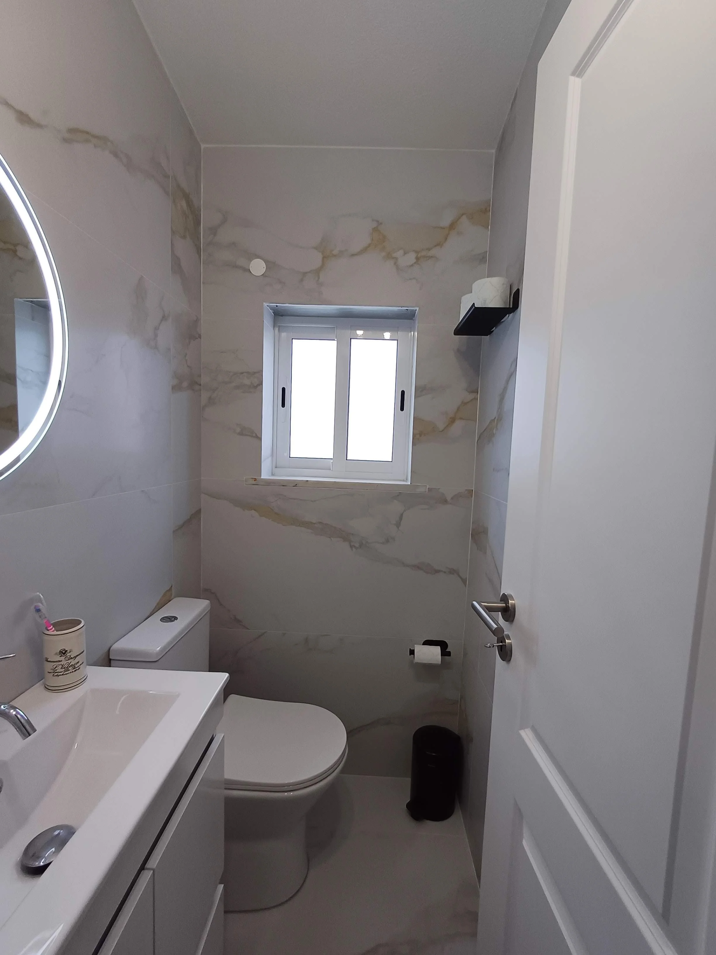 Remodelação de Casa de Banho Social, Mafra.
Casa-de-Banho Social com paredes efeito mármore. Torneiras e acessórios em preto. Armário branco brilho com gavetas e espelho redondo com iluminação periférica.