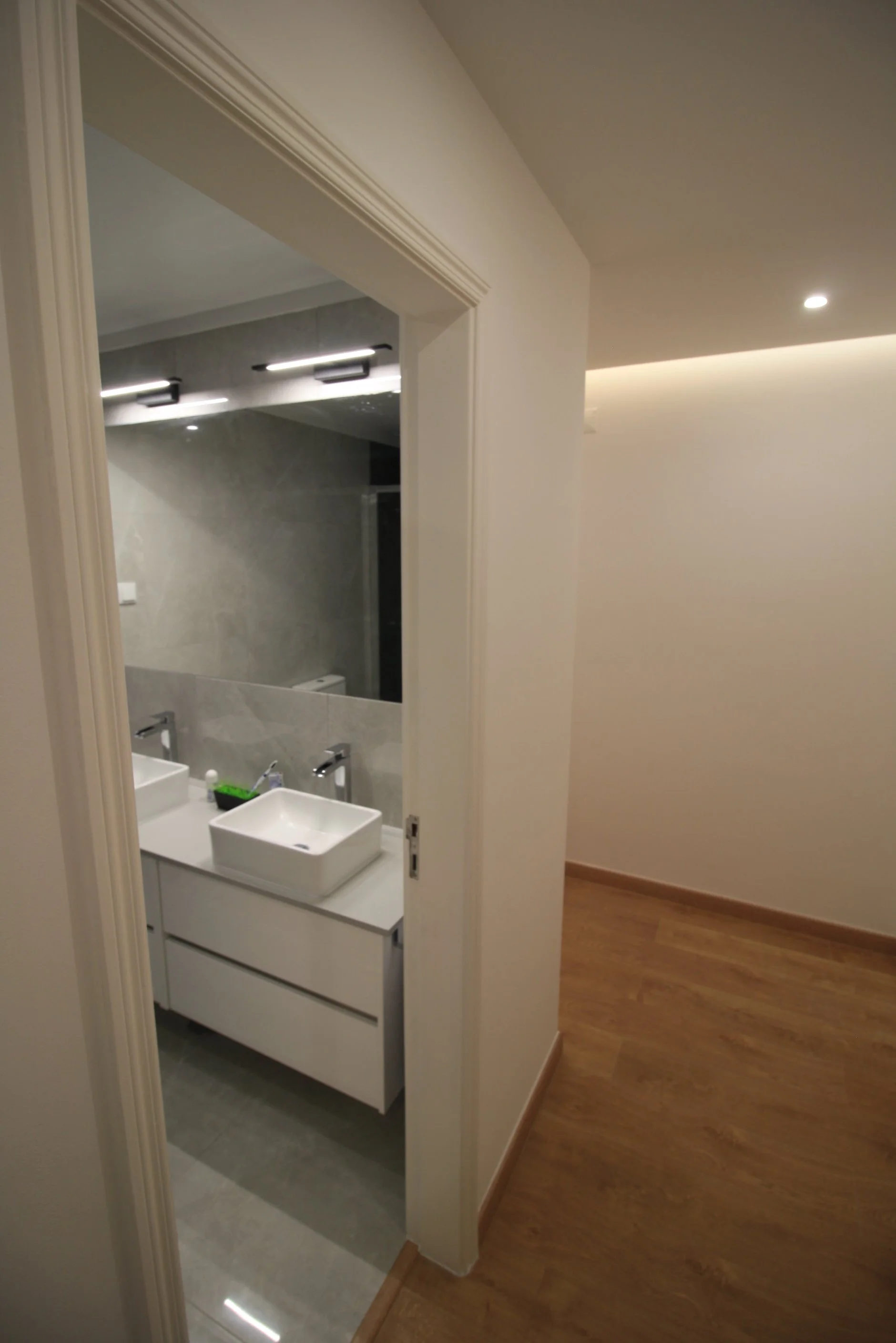 Corredor com sanca de luz para iluminação direta. Casa de banho com lavatório duplo e espelho de grande formato