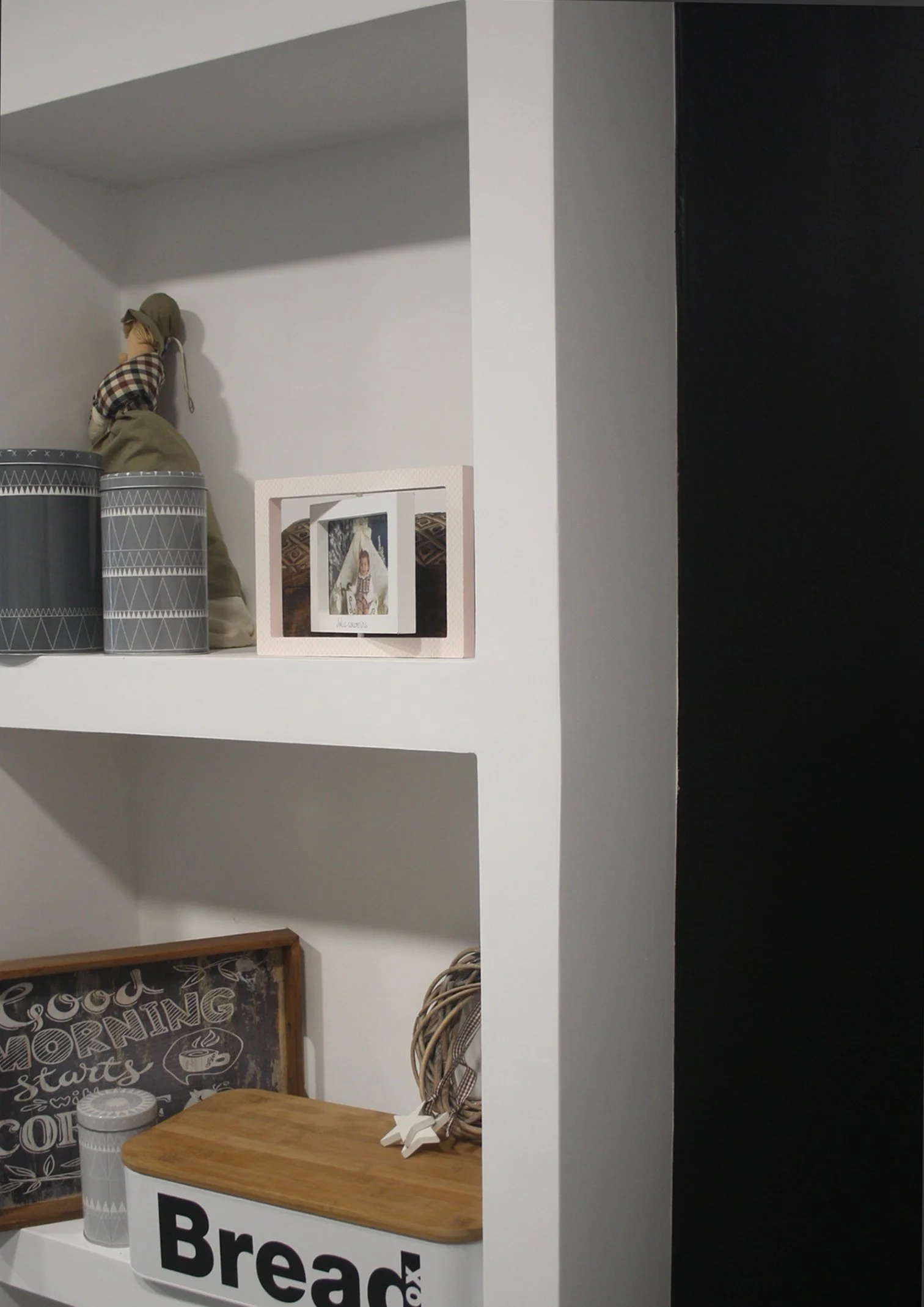 Prateleira branca com objetos decorativos, como latas decorativas, uma caixa de madeira com a palavra 'Bread' e uma placa com 'Good Morning' e mensagem de boas-vindas.