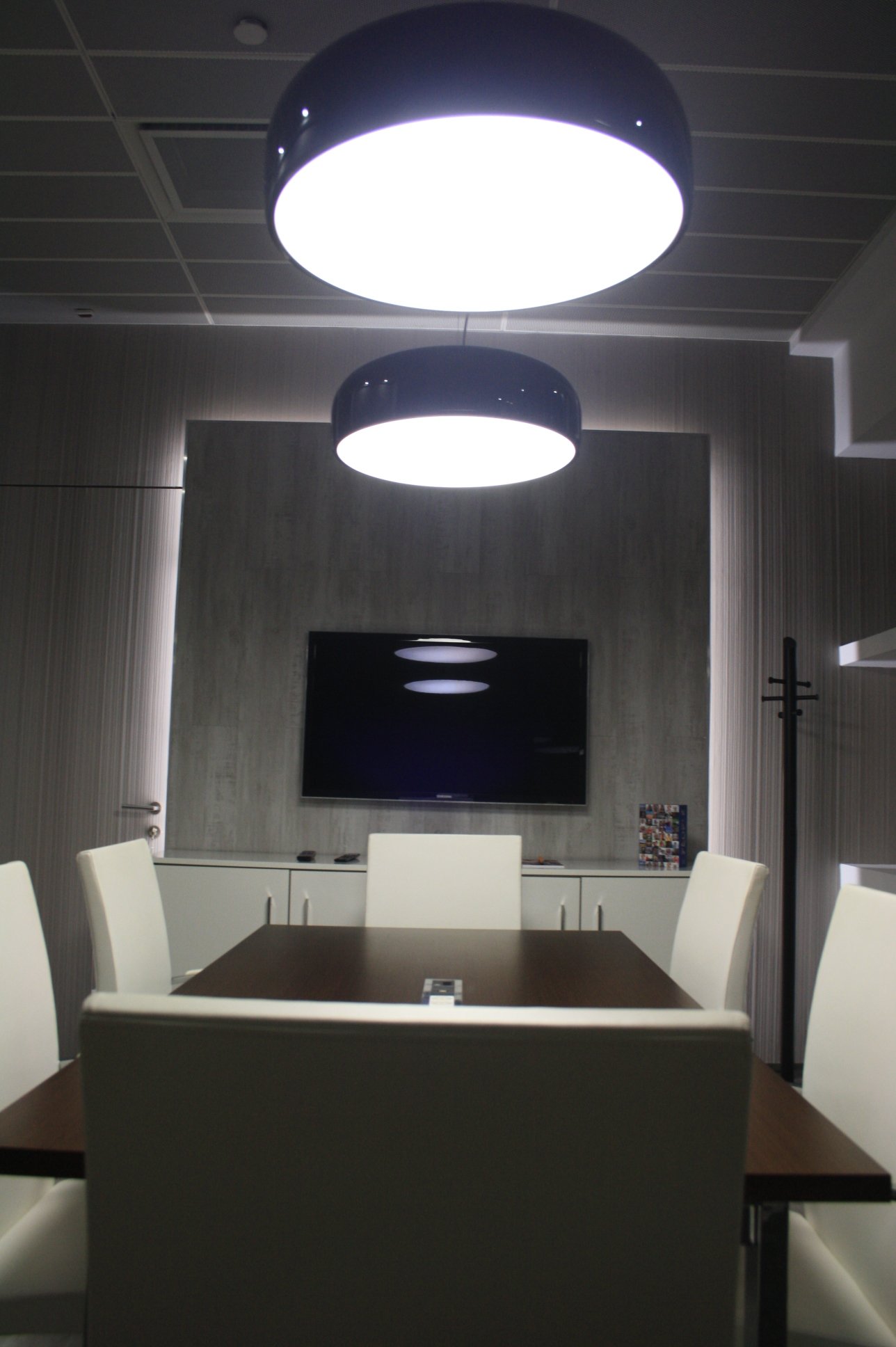 Sala de reuniões com painel retroiluminado, candeeiros de teto e cadeiras estofadas a pele branca.