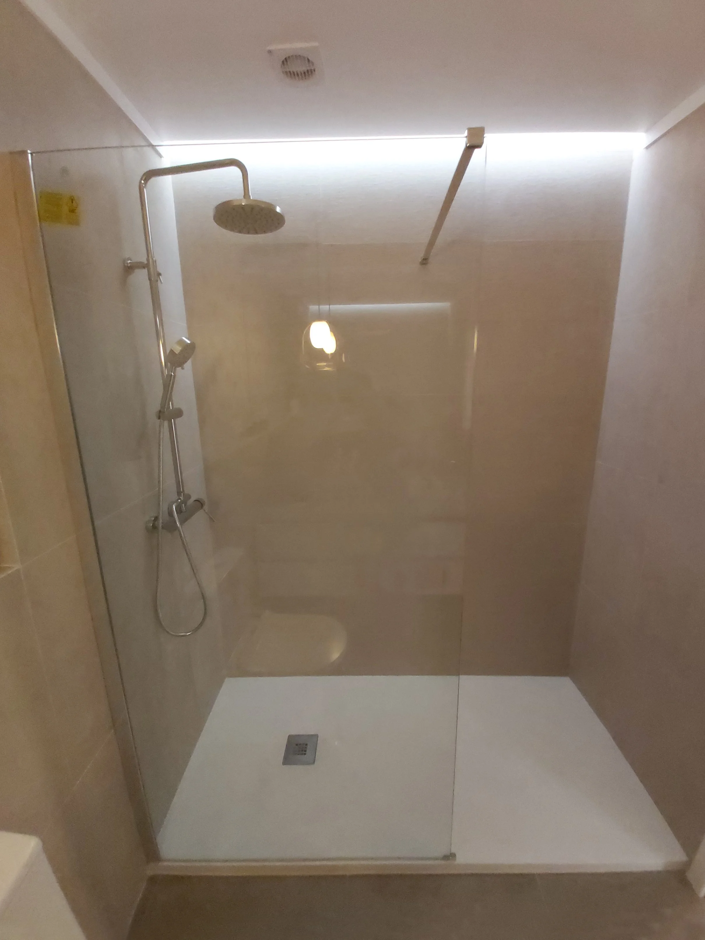 Box de banho com duas duchas, uma maior com cabeça redonda e uma menor, na parede de um banheiro com parede de azulejos bege e piso branco.