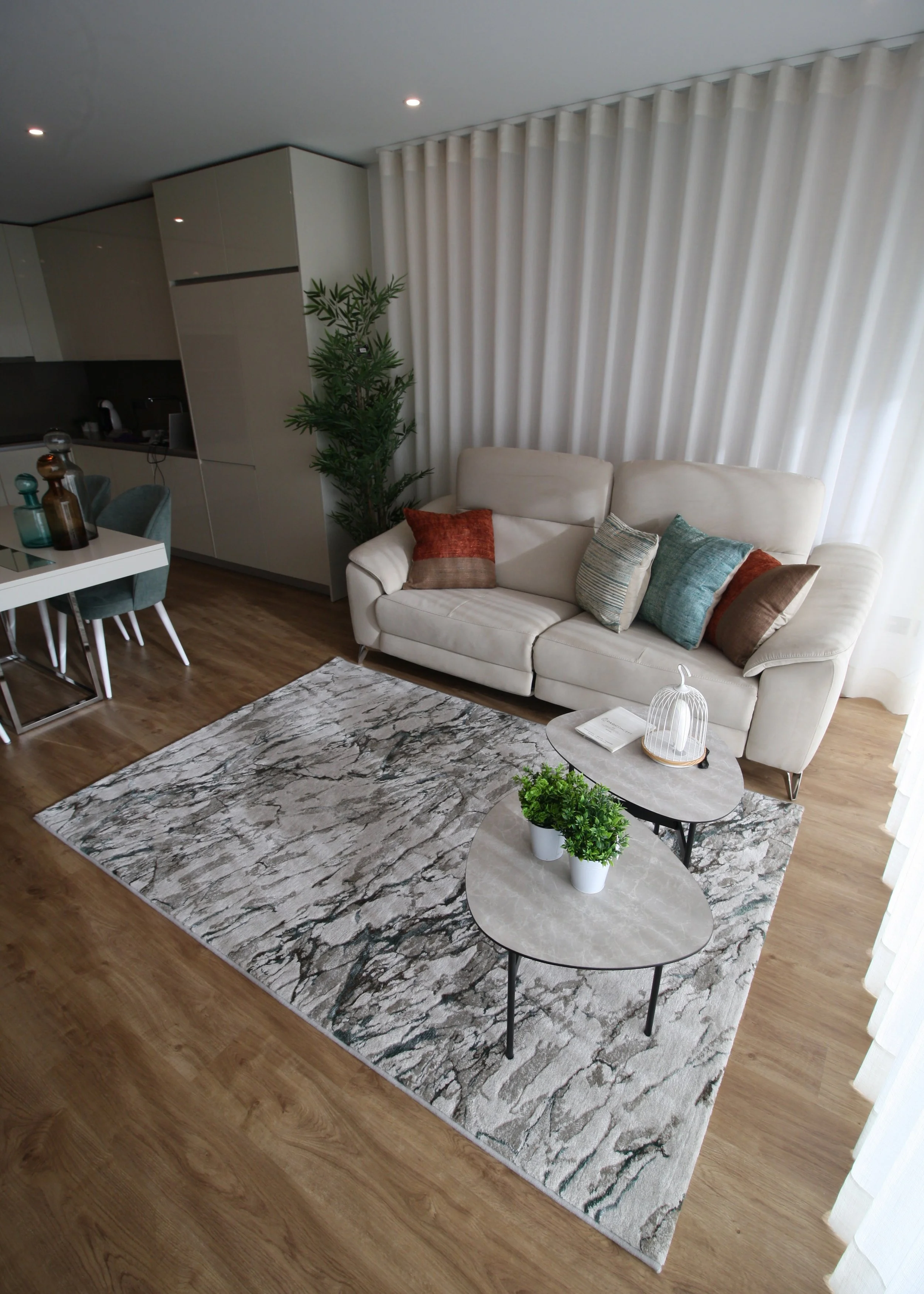 Decoração de Apartamento, Quarteira, Algarve.
Perspectiva de Sala. Sofá em pele com almofadas de tons tijolo e azul, tapete de padrão abstrato e mesas de apoio com tampos ovalizados de acabamento em micro-cimento.