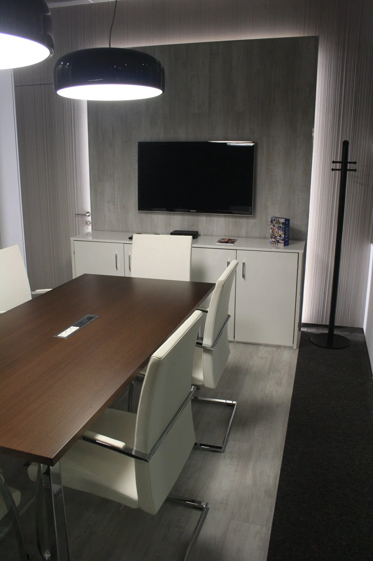 Sala de reuniões com painel retroiluminado, candeeiros de teto e cadeiras estofadas a pele branca.