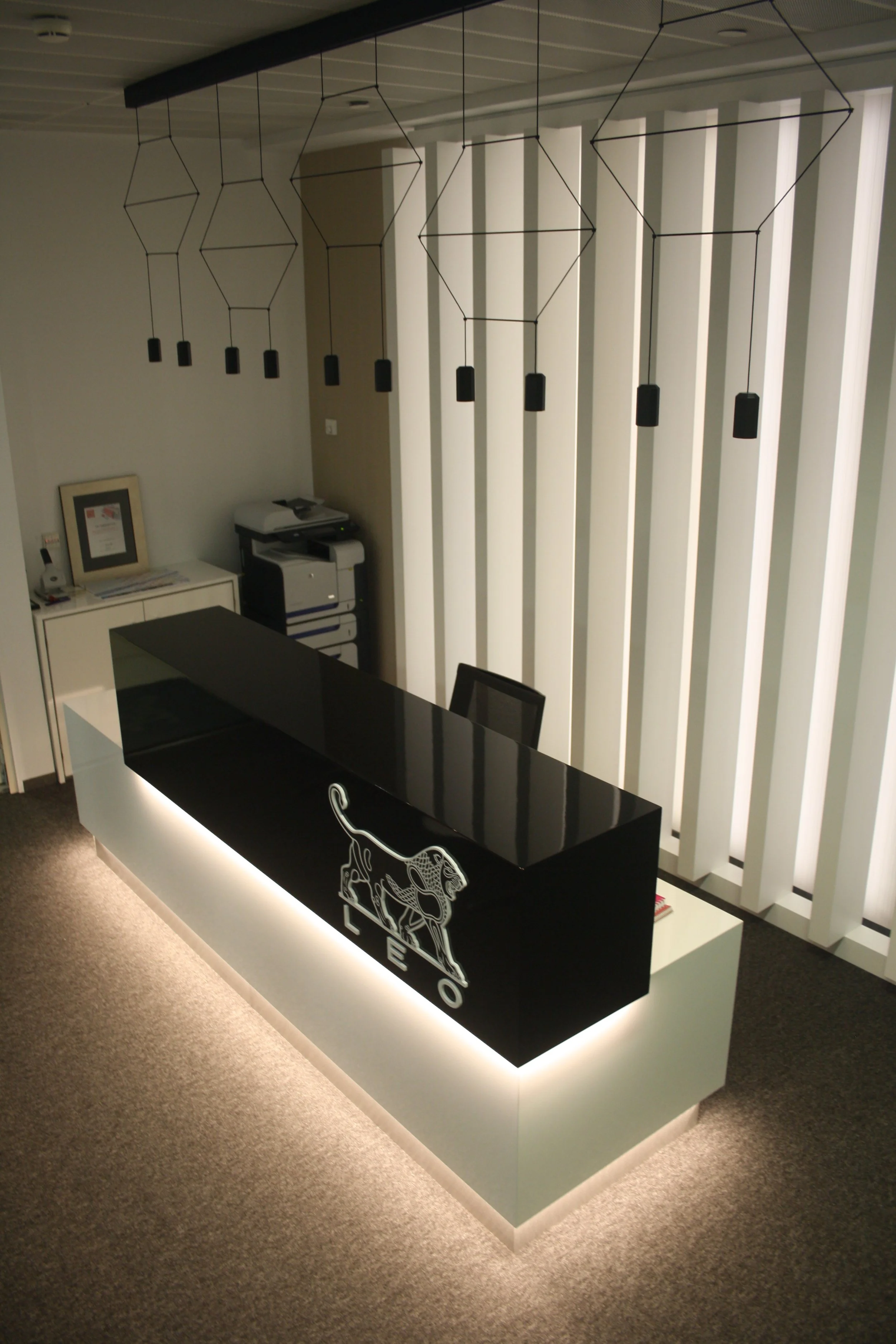 Balcão de recepção com iluminação integrada, candeeiro suspenso e painel ripado retro iluminado.