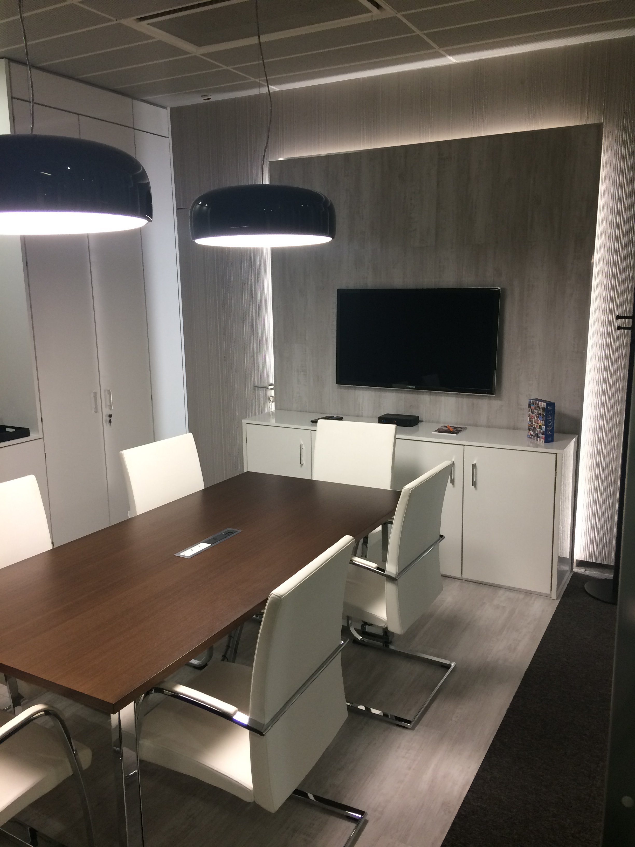 Sala de reuniões com painel retroiluminado, candeeiros de teto e cadeiras estofadas a pele branca