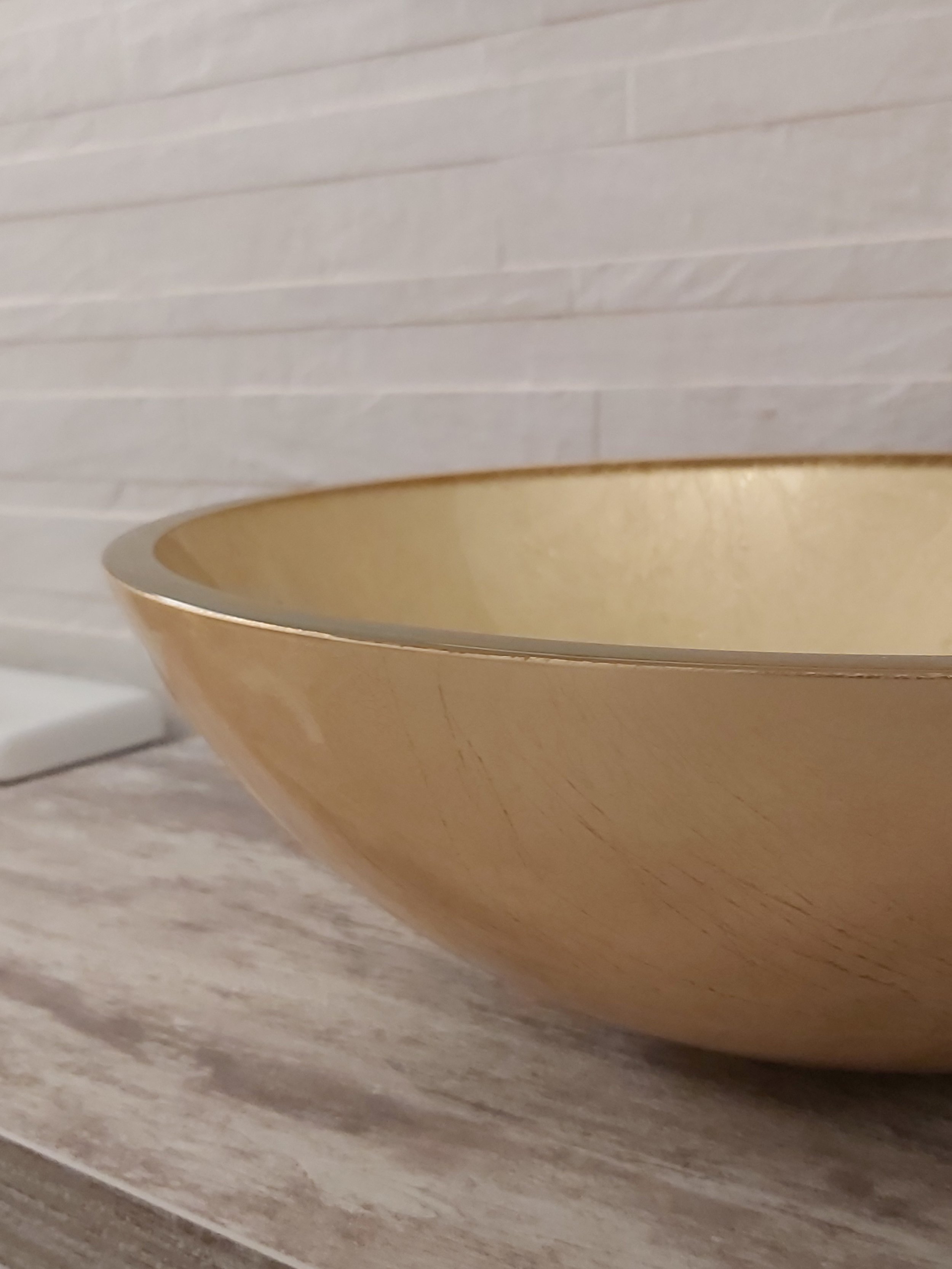  tigela dourada na bancada de mármore com parede de azulejos branca ao fundo