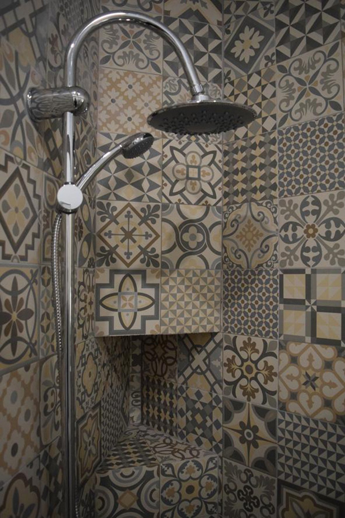 Chuveiro com teto de ducha em uma parede decorada com azulejos de padrão geométrico e floral em cores bege, cinza, preto e branco.