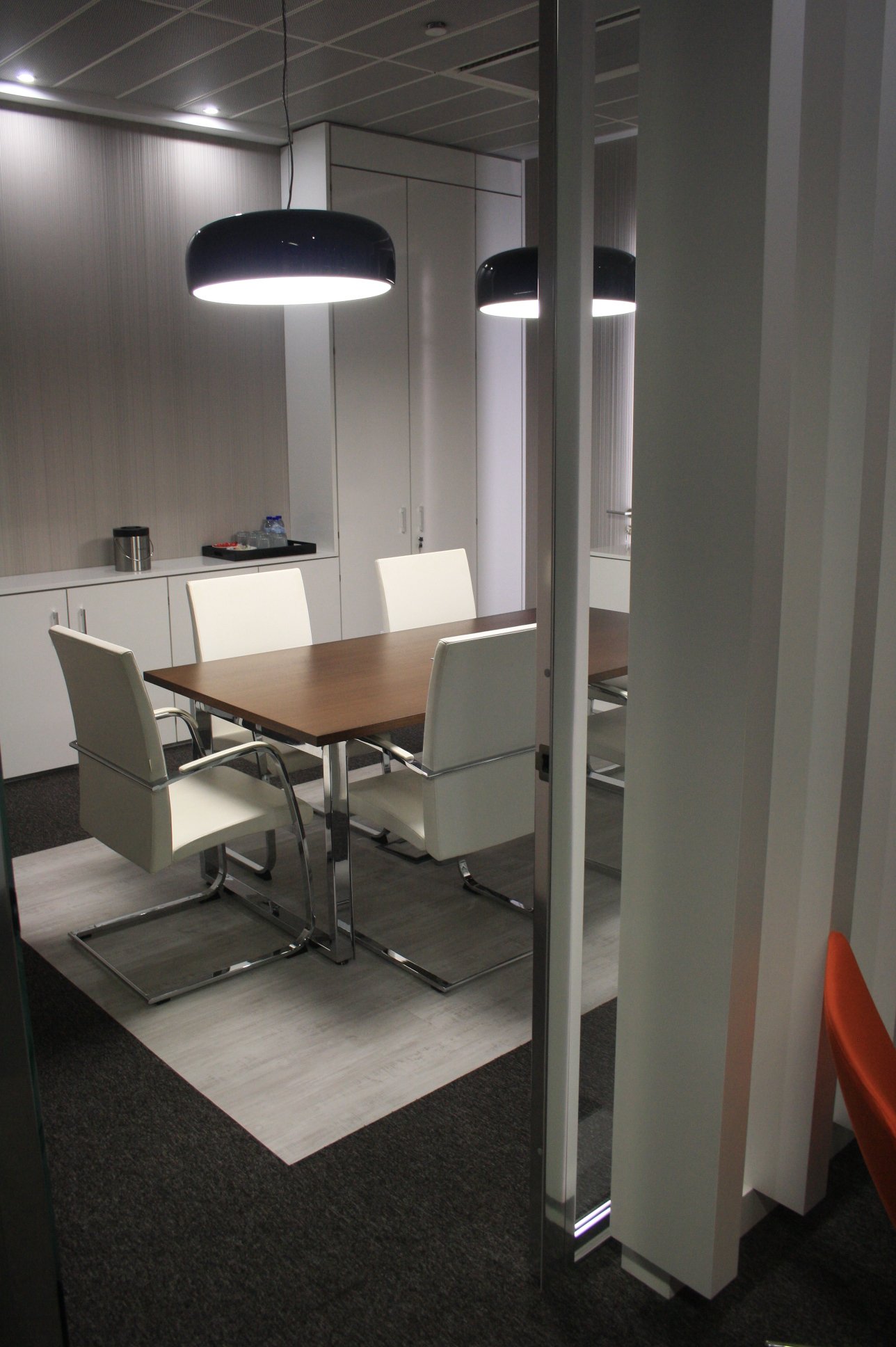 Sala de reuniões com painel retroiluminado, candeeiros de teto e cadeiras estofadas a pele branca.