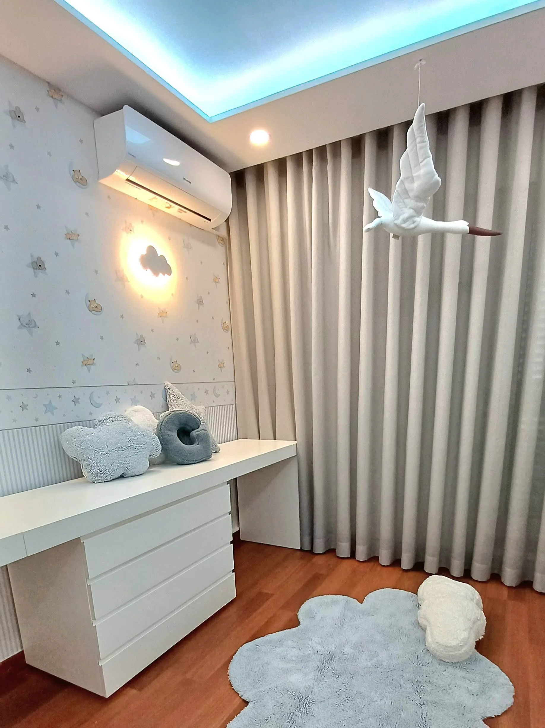 Quarto de bebê com tapete de nuvem, cortinas cinza, parede decorada com estrelas, nuvens e animais, e um móbile com gaivota no teto.