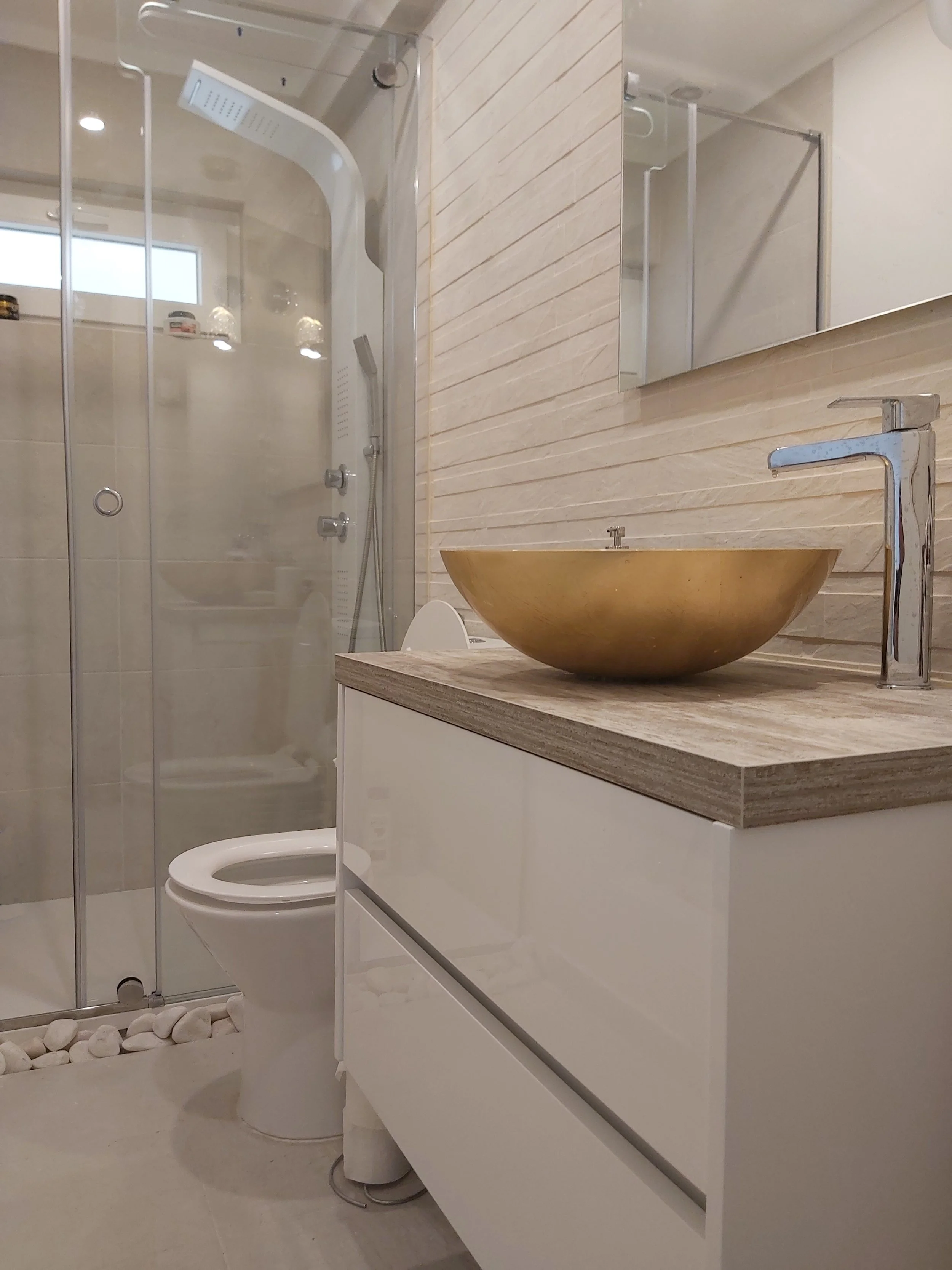 Banheiro com ducha, vaso sanitário, espelho e pia com cuba dourada.