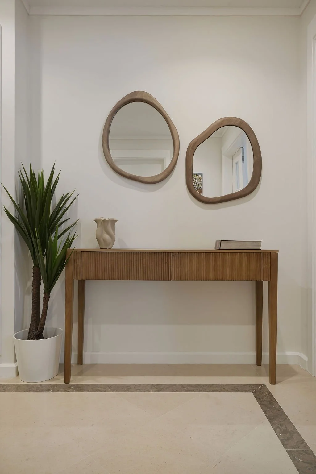Hall de entrada com móvel de madeira, vaso com planta, dois espelhos de parede de formato irregular de cariz rústico.