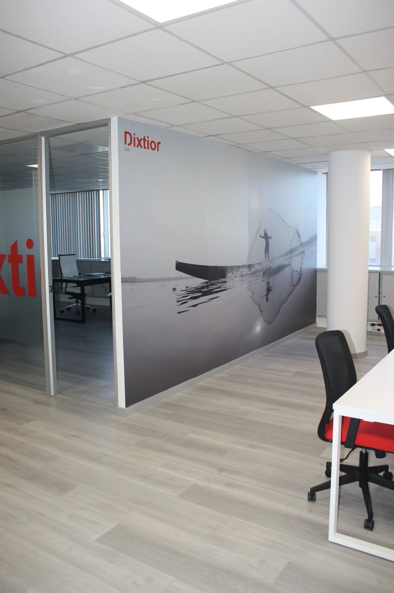 Escritório com uma parede decorativa de grande dimensão, que exibe uma foto de uma pessoa de barco ao pôr do sol ou amanhecer, e cabeças de mesa com cadeiras em primeiro plano.