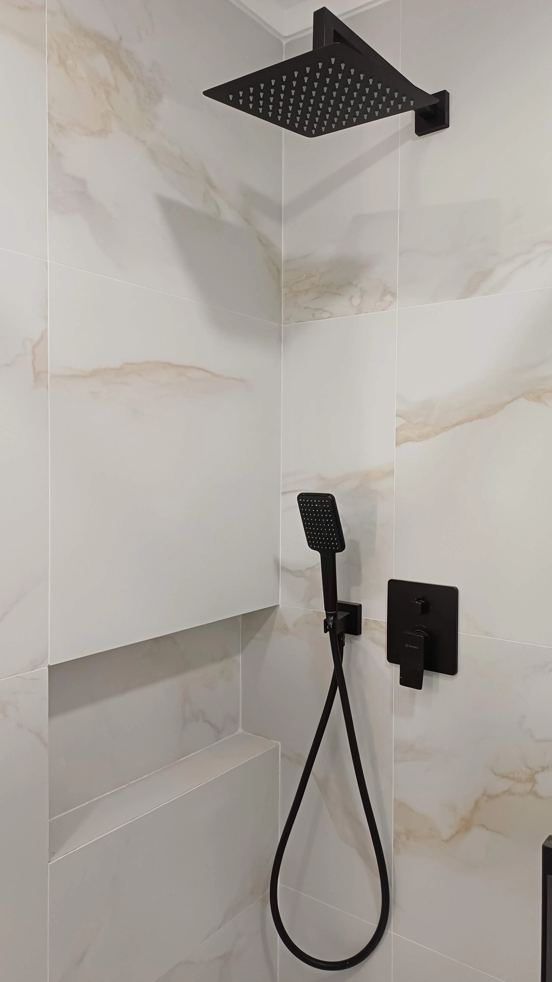 Chuveiro de ducha moderna com teto de chuveiro quadrado e mão de chuveiro com acabamento preto, instalado em parede de azulejos de mármore