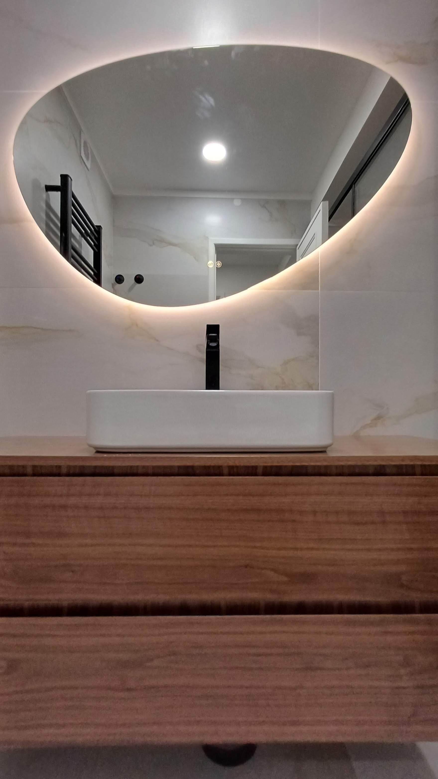 Projeto de Interiores e Remodelação de Apartamento, Queluz.
Remodelação de Casa-de-Banho com revestimento marmoreado de laivos dourados, Armário suspenso em madeira de Sucupira, base de duche em carga mineral, acessórios em preto e espelho de forma o