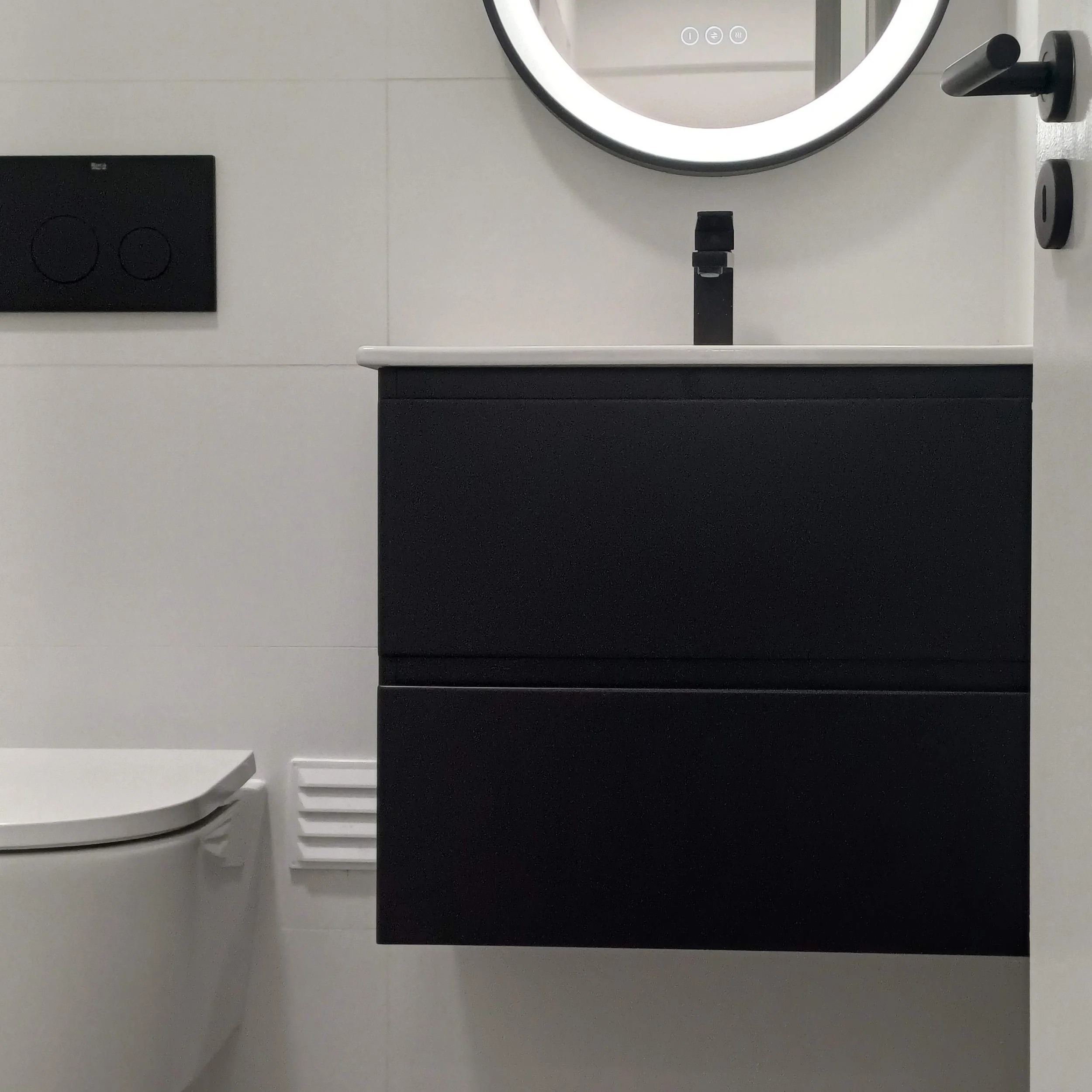 Decoração de Apartamento no Parque das Nações, Lisboa. Casa-de-Banho com Decoração Preto/Branco, Espelho com iluminação LED integrada, acessórios e botão de descarga de sanita suspensa de cor preta.