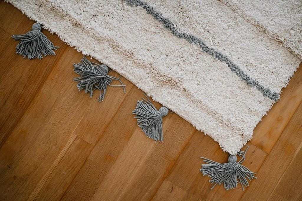 Tapete branco com detalhes cinza e pontas de cordão com franjas na casa de madeira.