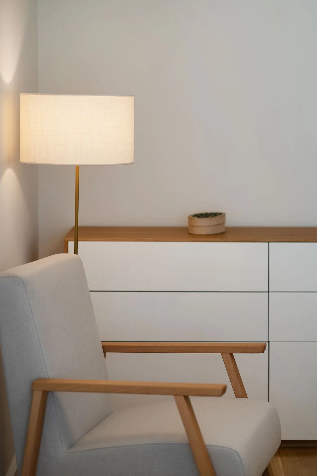 Candeeiro de pé, poltrona e móvel branco com tampo de madeira.