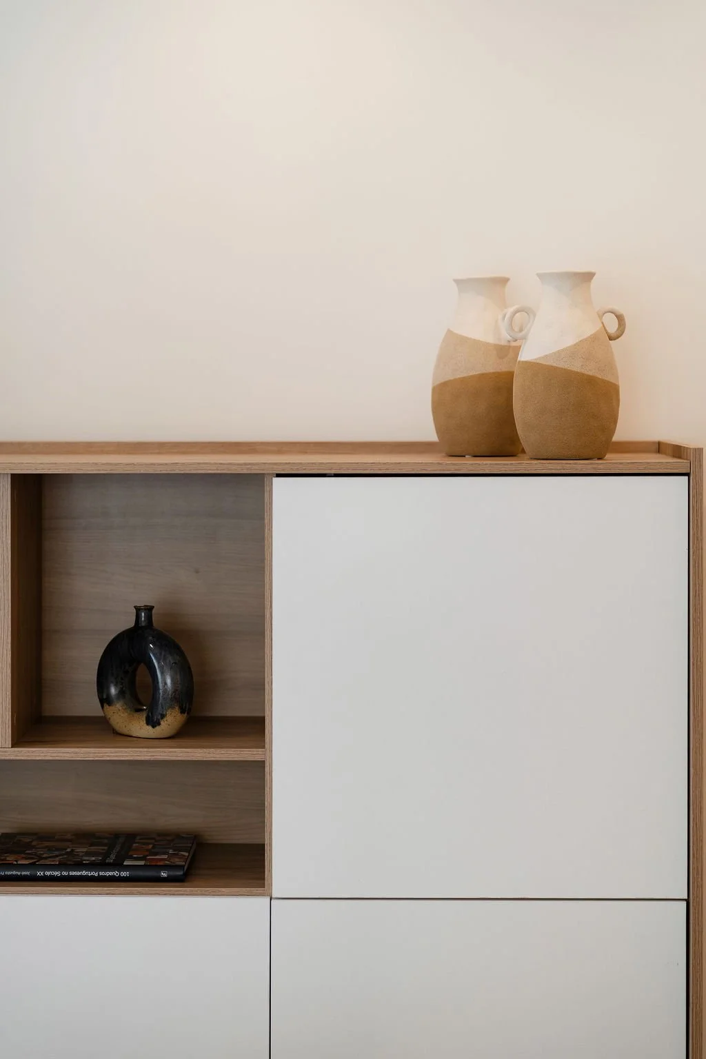 2 vasos cerâmicos bege e branca sobre móvel de madeira com frentes brancas.