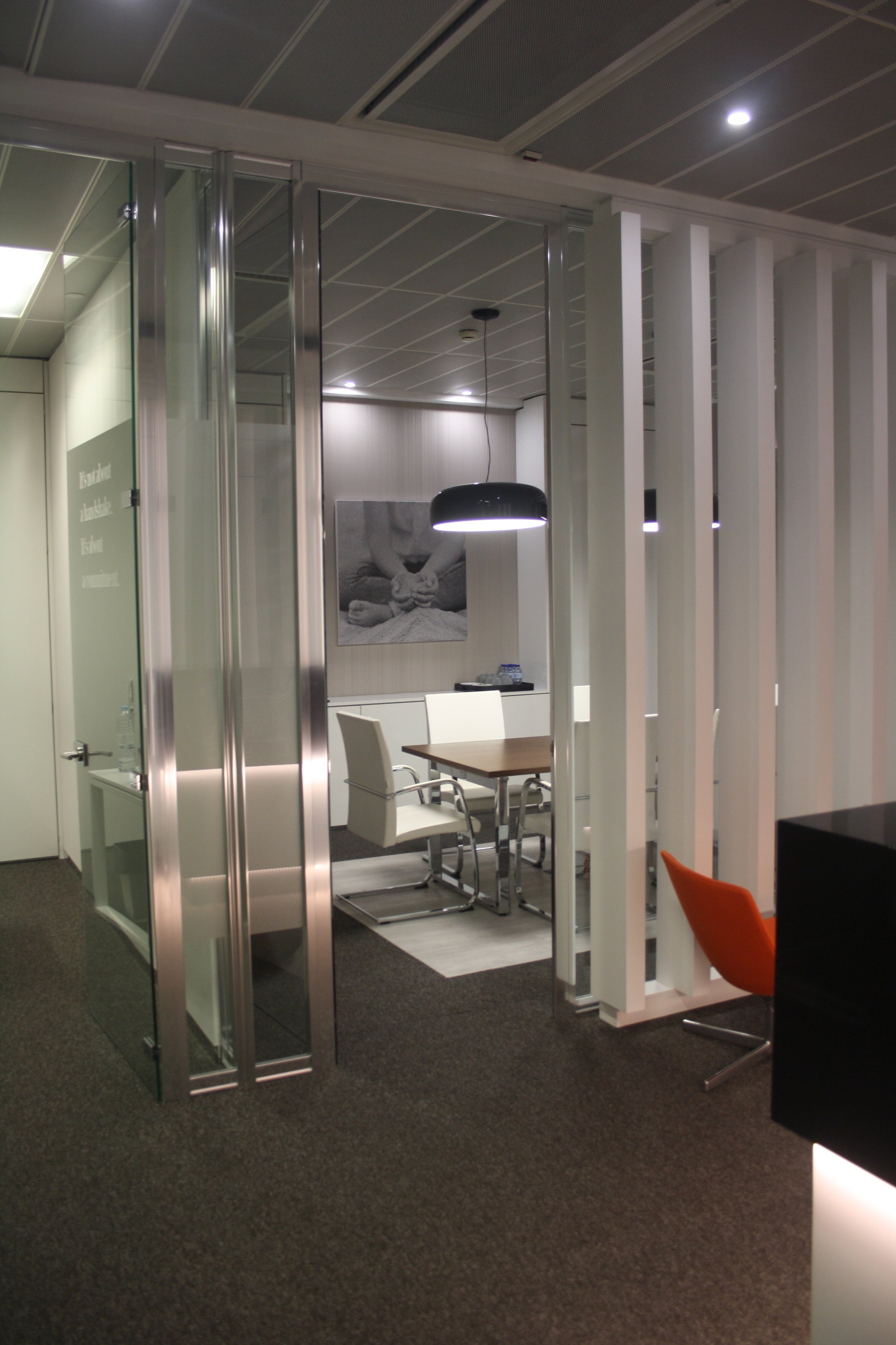 Acesso a Sala de reuniões com painel retroiluminado, candeeiros de teto e cadeiras estofadas a pele branca.