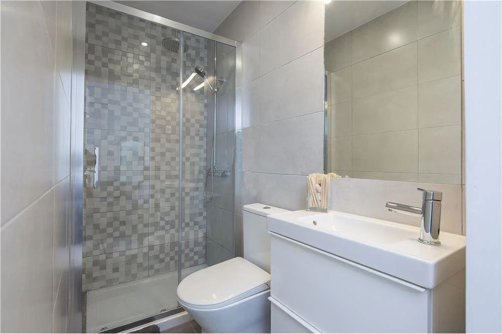 Banheiro com ducha de vidro, vaso sanitário e lavatório compacto com espelho grande na parede