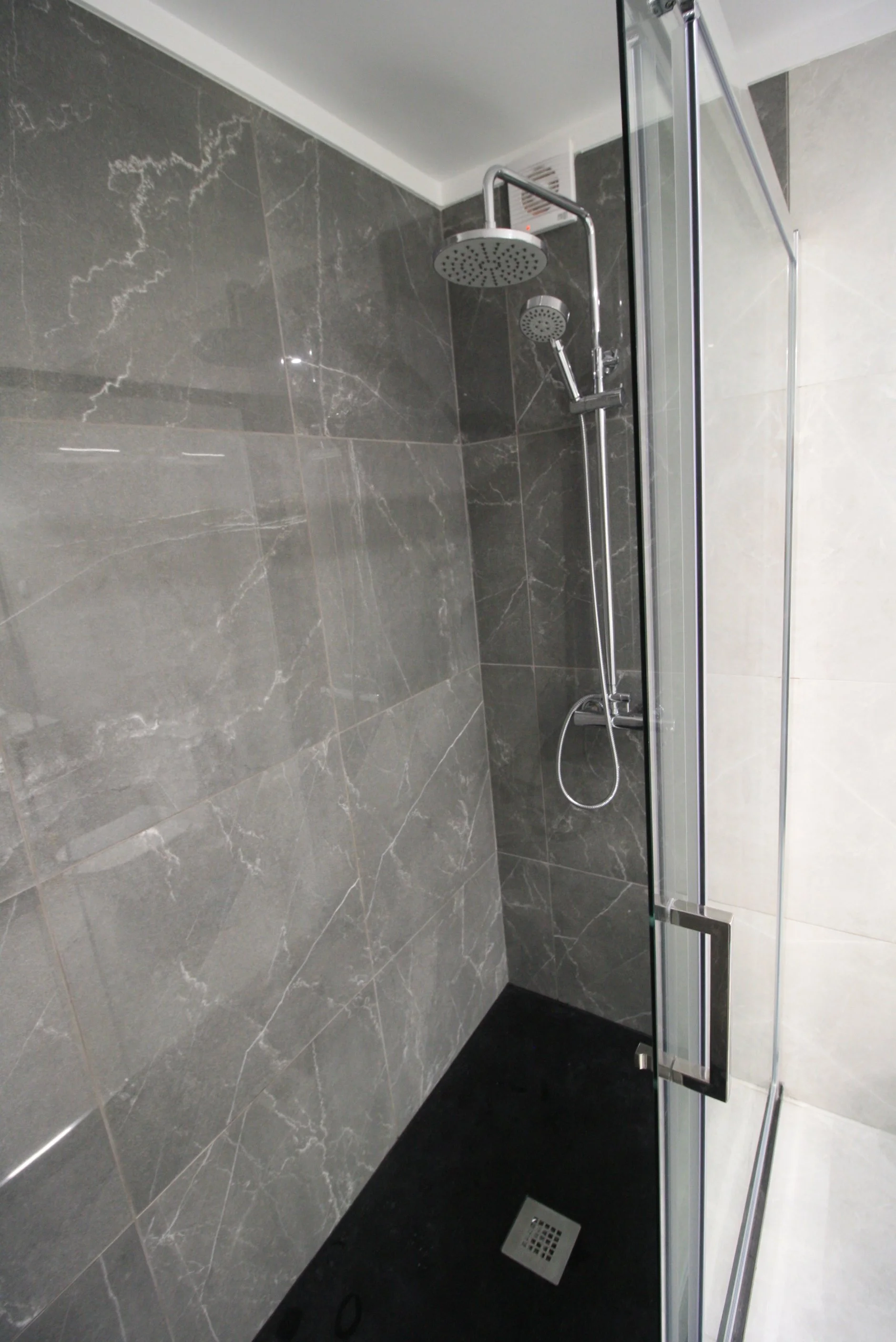 Casa de banho com revestimento de cor branca e com cabine de duche duplo e marcação de área de duche com revestimento cerâmico de cor preta