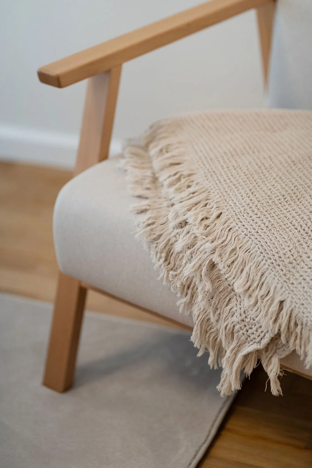 Poltrona de madeira estofada a branco, coberta por uma manta bege. Tapete cinza claro.
